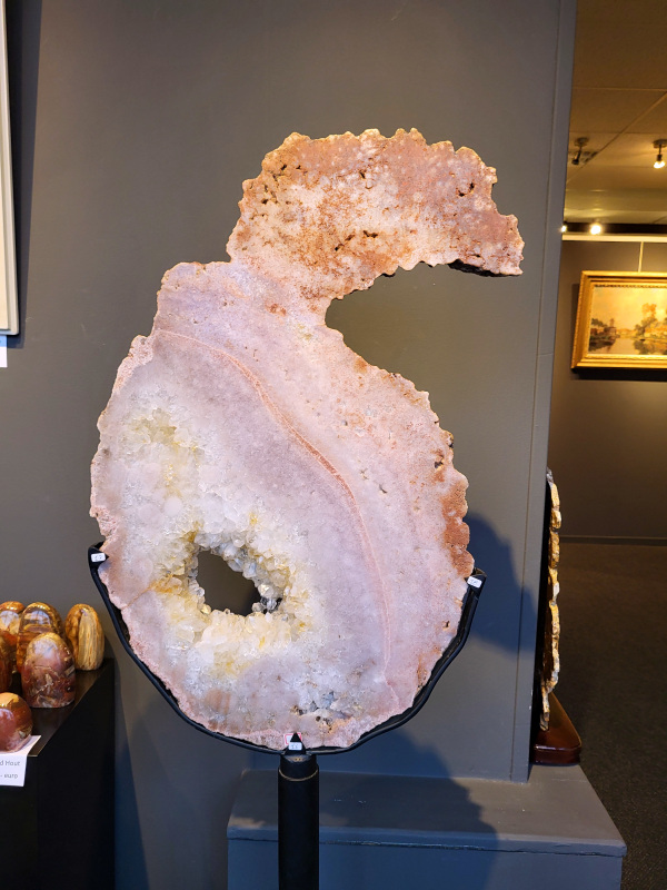 Roze Amethist, Chalcedoon, 26kg, 155cm hoog, 75cm doorsnee, 990,- euro, nr. 21

Chalcedoon, ook wel genoemd Roze Amethist

Chalcedoon is een edelsteen die behoort tot de kwartsfamilie en bekend staat om zijn zachte, wasachtige glans en diverse kleuren. Het is een microkristallijne vorm van kwarts, vaak in wit, grijs, blauw, geel, bruin of rood. Chalcedoon wordt gewaardeerd om zijn spirituele eigenschappen, zoals het bevorderen van communicatie, evenwicht en creativiteit. 
Kenmerken en soorten:
Chalcedoon is een cryptokristal gelijnde  kwarts, wat betekent dat de kristallen zo klein zijn dat ze met het blote oog niet te zien zijn. 
Het heeft een hardheid van 6,5-7 op de schaal van Mohs. 
Bekende variëteiten van chalcedoon zijn chrysopraas (appelgroen), carneool (roze tot rood) en sarder (bruin). 
Blauwe chalcedoon, met name Blue Lace Agate, staat bekend om zijn kalmerende werking en wordt geassocieerd met de keelchakra. 
Spirituele eigenschappen en werking:
Chalcedoon wordt gezien als de steen van communicatie en wordt vaak de "redenaarssteen" genoemd. 
Het bevordert helderheid van geest, zelfvertrouwen en moed om gevoelens te uiten. 
Chalcedoon kan helpen bij het loslaten van onderdrukte emoties en het vinden van innerlijke rust. 
Het wordt ook in verband gebracht met creativiteit en het vermogen om ideeën om te zetten in daden. 
Sommige geloven dat chalcedoon het keelchakra activeert en helpt bij problemen met de keel, stembanden en schildklier. 
Fysieke werking:
Chalcedoon wordt verondersteld reinigende, verkoelende en ontstekingsremmende eigenschappen te hebben.
Het kan helpen bij koorts, verkoudheid, ademhalingsproblemen en het versterken van het immuunsysteem. 
Chalcedoon wordt ook in verband gebracht met een positieve werking op de bloedsomloop, vochtophoping en de productie van insuline.
Overige:
Chalcedoon komt voor in verschillende delen van de wereld, waaronder Brazilië, Madagaskar, India en Uruguay. 
In de oudheid werd chalcedoon al gebruikt voor amuletten, zegels en sieraden.