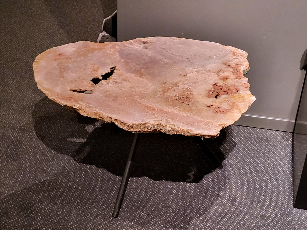 Roze Amethist, Chalcedoon, Tafel, 24,6kg, 75cm, doorsnee 750,- euro, nr. 60

Chalcedoon, ook wel genoemd Roze Amethist

Chalcedoon is een edelsteen die behoort tot de kwartsfamilie en bekend staat om zijn zachte, wasachtige glans en diverse kleuren. Het is een microkristallijne vorm van kwarts, vaak in wit, grijs, blauw, geel, bruin of rood. Chalcedoon wordt gewaardeerd om zijn spirituele eigenschappen, zoals het bevorderen van communicatie, evenwicht en creativiteit. 
Kenmerken en soorten:
Chalcedoon is een cryptokristal gelijnde  kwarts, wat betekent dat de kristallen zo klein zijn dat ze met het blote oog niet te zien zijn. 
Het heeft een hardheid van 6,5-7 op de schaal van Mohs. 
Bekende variëteiten van chalcedoon zijn chrysopraas (appelgroen), carneool (roze tot rood) en sarder (bruin). 
Blauwe chalcedoon, met name Blue Lace Agate, staat bekend om zijn kalmerende werking en wordt geassocieerd met de keelchakra. 
Spirituele eigenschappen en werking:
Chalcedoon wordt gezien als de steen van communicatie en wordt vaak de "redenaarssteen" genoemd. 
Het bevordert helderheid van geest, zelfvertrouwen en moed om gevoelens te uiten. 
Chalcedoon kan helpen bij het loslaten van onderdrukte emoties en het vinden van innerlijke rust. 
Het wordt ook in verband gebracht met creativiteit en het vermogen om ideeën om te zetten in daden. 
Sommige geloven dat chalcedoon het keelchakra activeert en helpt bij problemen met de keel, stembanden en schildklier. 
Fysieke werking:
Chalcedoon wordt verondersteld reinigende, verkoelende en ontstekingsremmende eigenschappen te hebben.
Het kan helpen bij koorts, verkoudheid, ademhalingsproblemen en het versterken van het immuunsysteem. 
Chalcedoon wordt ook in verband gebracht met een positieve werking op de bloedsomloop, vochtophoping en de productie van insuline.
Overige:
Chalcedoon komt voor in verschillende delen van de wereld, waaronder Brazilië, Madagaskar, India en Uruguay. 
In de oudheid werd chalcedoon al gebruikt voor amuletten, zegels en sieraden.