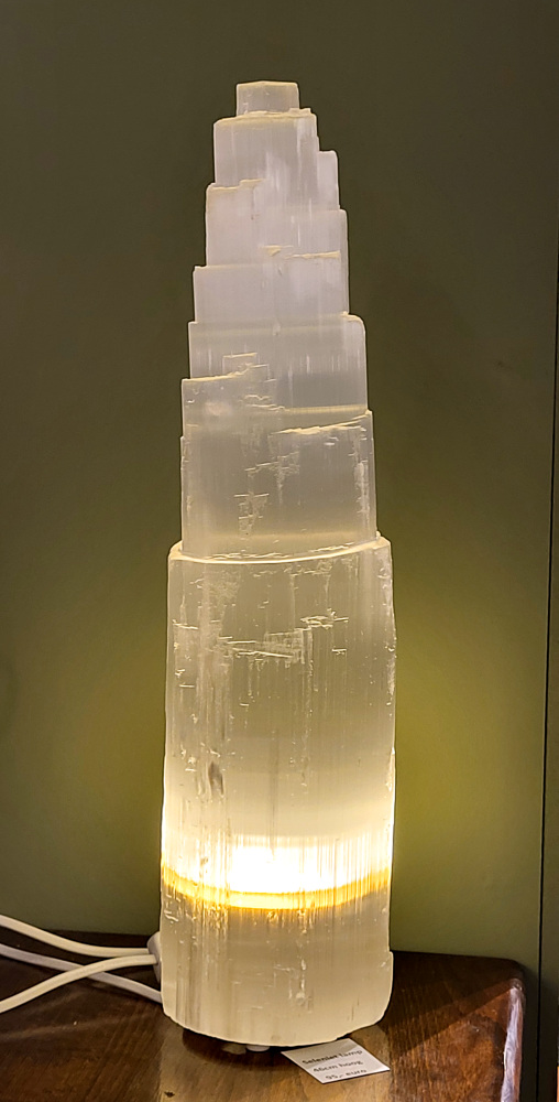 Seleniet lamp, XXL, 46cm hoog, 95,- euro, nr. 50

Seleniet is een kristallijne vorm van gips, ook wel satijnspaat genoemd, bekend om zijn zuiverende en spirituele eigenschappen. Het mineraal is relatief zacht, is te vinden in verschillende kleuren (wit, oranje, geel, groen) en wordt vaak gebruikt bij healing en meditatie. Seleniet wordt spiritueel geassocieerd met rust, heling en het reinigen van energie, en het staat bekend om zijn zelfreinigende en het reinigen van andere stenen. 
Eigenschappen en uiterlijk
Samenstelling: Seleniet is een gehydrateerd calciumsulfaat en een variant van gips.
Hardheid: Met een hardheid van 2 is het een zachte steen.
Vorm: Het komt vaak voor in lange, heldere, tabulaire kristallen met een vezelige structuur.
Kleur: De kleur kan variëren, maar de meest voorkomende kleuren zijn wit, kleurloos, geel, oranje en groen. De witte variant wordt vaak satijnspaat genoemd.
Bijzonderheden: Sommige selenietkristallen kunnen flexibel zijn en enhydrokristallen kunnen kleine water- en gasbelletjes bevatten. 
Spirituele betekenis en gebruik
Reiniging: Seleniet wordt beschouwd als een krachtige zuiveraar die negatieve energie verwijdert en harmonie brengt.
Healing en meditatie: Het wordt vaak gebruikt tijdens meditatie, healing en voor het communiceren met hogere sferen.
Zelfreinigend: Seleniet is een zelfreinigende steen en wordt vaak gebruikt om andere edelstenen energetisch op te laden.
Chakra's: Het is sterk verbonden met de kruin- en derde-oogchakra, wat helpt bij spiritueel bewustzijn en intuïtie.
Spirituele namen: Het wordt ook wel "engelensteen" genoemd vanwege de hoge vibratie die heling en transformatie brengt. 
Verzorging
Vermijd water: Omdat het een gipsvariant is, mag seleniet nooit worden gereinigd met water, aangezien het kan oplossen of beschadigen.
Reinigingsmethodes: Reinig het energetisch met rook van salie of palo santo, of door het op een cluster van amethist of hematiet te plaatsen.
Opladen: Om seleniet op te laden, kan maanlicht of een bergkristal worden gebruikt.