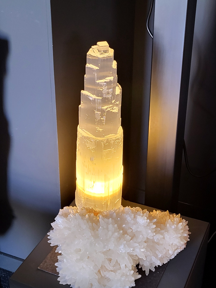 Seleniet lamp, 46cm hoog, XXL formaat, 95,- euro, nr. 52

Seleniet is een kristallijne vorm van gips, ook wel satijnspaat genoemd, bekend om zijn zuiverende en spirituele eigenschappen. Het mineraal is relatief zacht, is te vinden in verschillende kleuren (wit, oranje, geel, groen) en wordt vaak gebruikt bij healing en meditatie. Seleniet wordt spiritueel geassocieerd met rust, heling en het reinigen van energie, en het staat bekend om zijn zelfreinigende en het reinigen van andere stenen. 
Eigenschappen en uiterlijk
Samenstelling: Seleniet is een gehydrateerd calciumsulfaat en een variant van gips.
Hardheid: Met een hardheid van 2 is het een zachte steen.
Vorm: Het komt vaak voor in lange, heldere, tabulaire kristallen met een vezelige structuur.
Kleur: De kleur kan variëren, maar de meest voorkomende kleuren zijn wit, kleurloos, geel, oranje en groen. De witte variant wordt vaak satijnspaat genoemd.
Bijzonderheden: Sommige selenietkristallen kunnen flexibel zijn en enhydrokristallen kunnen kleine water- en gasbelletjes bevatten. 
Spirituele betekenis en gebruik
Reiniging: Seleniet wordt beschouwd als een krachtige zuiveraar die negatieve energie verwijdert en harmonie brengt.
Healing en meditatie: Het wordt vaak gebruikt tijdens meditatie, healing en voor het communiceren met hogere sferen.
Zelfreinigend: Seleniet is een zelfreinigende steen en wordt vaak gebruikt om andere edelstenen energetisch op te laden.
Chakra's: Het is sterk verbonden met de kruin- en derde-oogchakra, wat helpt bij spiritueel bewustzijn en intuïtie.
Spirituele namen: Het wordt ook wel "engelensteen" genoemd vanwege de hoge vibratie die heling en transformatie brengt. 
Verzorging
Vermijd water: Omdat het een gipsvariant is, mag seleniet nooit worden gereinigd met water, aangezien het kan oplossen of beschadigen.
Reinigingsmethodes: Reinig het energetisch met rook van salie of palo santo, of door het op een cluster van amethist of hematiet te plaatsen.
Opladen: Om seleniet op te laden, kan maanlicht of een bergkristal worden gebruikt.