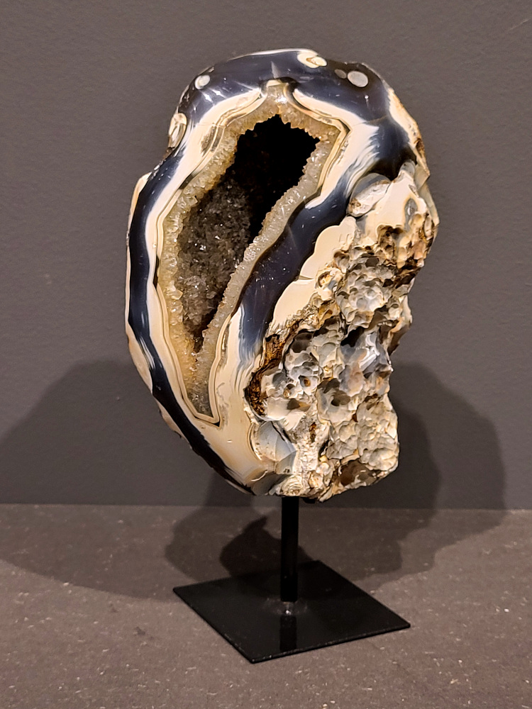 <strong>Agaat, Cluster,Geode,Agaat op standaard, 1,2kg, 20cm hoog, 61euro, nr. 50</strong>

<strong>Beschrijving Agaat.</strong>

Agaat is een veelzijdige edelsteen die bekend staat om zijn prachtige kleurbanden en patronen. Het is een variëteit van het mineraal kwarts, meer specifiek chalcedoon, en wordt vaak gebruikt in sieraden en als decoratieve steen. 
<strong>Algemene kenmerken:</strong>
Agaat is een microkristallijne vorm van kwarts, bestaande uit microscopisch kleine kristallen. 
<strong>Kleuren en patronen:</strong>
Agaat komt voor in vele kleuren, vaak met banden of lagen in verschillende tinten. 
Agaat is een populaire keuze voor het maken van kettingen, armbanden, ringen en andere sieraden vanwege de esthetische aantrekkingskracht en duurzaamheid. 
<strong>Spirituele eigenschappen:</strong>
Agaat wordt vaak geassocieerd met aardende, stabiliserende en beschermende eigenschappen. 
<strong>Helende werking:</strong>
Er wordt aangenomen dat agaat kan helpen bij het verminderen van stress, het bevorderen van emotioneel evenwicht en het versterken van het zelfvertrouwen. 
<strong>Verzorging van agaat:</strong>
Agaat is relatief gemakkelijk te onderhouden. Het kan worden gereinigd met lauw water, de rook van witte salie of palo santo, of door het op een hematiet- of bergkristal-cluster te plaatsen. 

<strong>-	Kunstgalerie-Arnold -</strong>