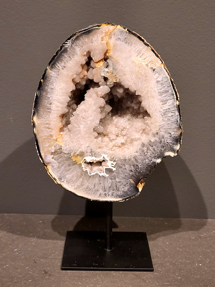 <strong>Agaat, Cluster, Geode, Agaat op standaard, 1,3kg, 20cm hoog, 66,- euro, nr. 51</strong>

<strong>Beschrijving Agaat.</strong>

Agaat is een veelzijdige edelsteen die bekend staat om zijn prachtige kleurbanden en patronen. Het is een variëteit van het mineraal kwarts, meer specifiek chalcedoon, en wordt vaak gebruikt in sieraden en als decoratieve steen. 
<strong>Algemene kenmerken:</strong>
Agaat is een microkristallijne vorm van kwarts, bestaande uit microscopisch kleine kristallen. 
<strong>Kleuren en patronen:</strong>
Agaat komt voor in vele kleuren, vaak met banden of lagen in verschillende tinten. 
Agaat is een populaire keuze voor het maken van kettingen, armbanden, ringen en andere sieraden vanwege de esthetische aantrekkingskracht en duurzaamheid. 
<strong>Spirituele eigenschappen:</strong>
Agaat wordt vaak geassocieerd met aardende, stabiliserende en beschermende eigenschappen. 
<strong>Helende werking:</strong>
Er wordt aangenomen dat agaat kan helpen bij het verminderen van stress, het bevorderen van emotioneel evenwicht en het versterken van het zelfvertrouwen. 
<strong>Verzorging van agaat:</strong>
Agaat is relatief gemakkelijk te onderhouden. Het kan worden gereinigd met lauw water, de rook van witte salie of palo santo, of door het op een hematiet- of bergkristal-cluster te plaatsen. 

<strong>-	Kunstgalerie-Arnold -</strong>