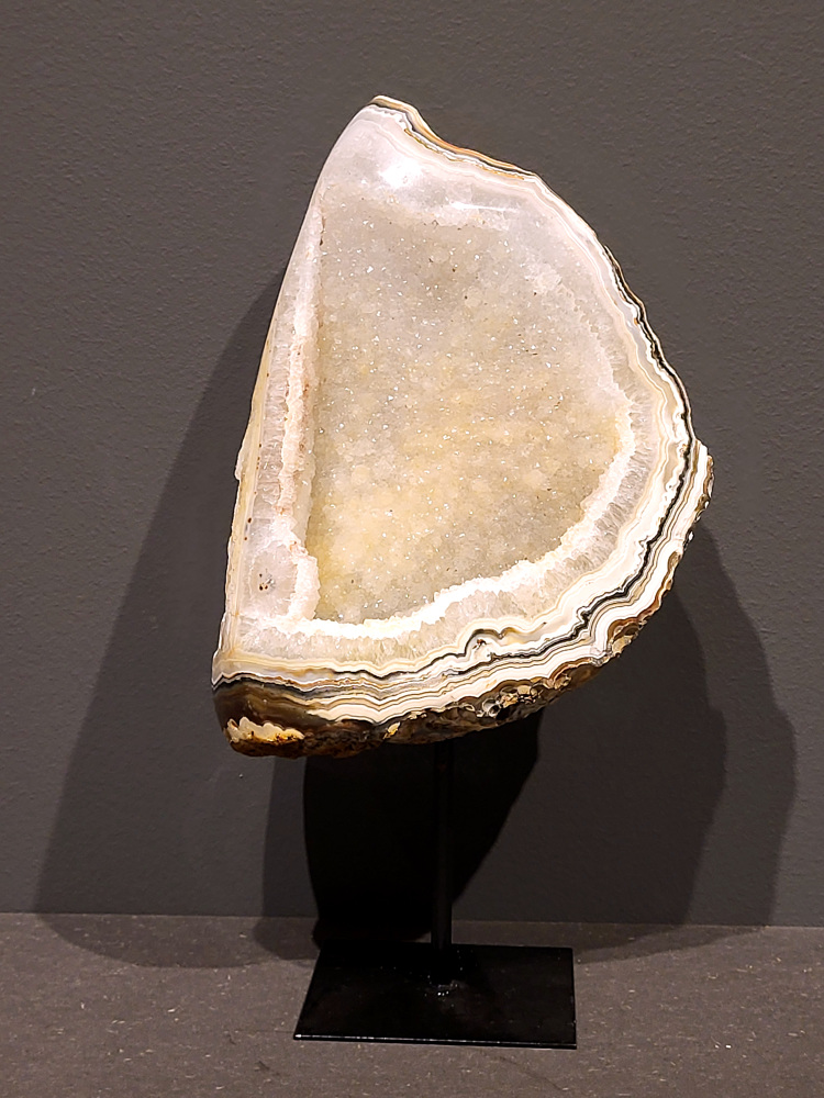 <strong>Agaat, Cluster, Geode, Agaat op standaard, 2,2kg, 28cm hoog, 108,- euro, nr. 52</strong>

<strong>Beschrijving Agaat.</strong>

Agaat is een veelzijdige edelsteen die bekend staat om zijn prachtige kleurbanden en patronen. Het is een variëteit van het mineraal kwarts, meer specifiek chalcedoon, en wordt vaak gebruikt in sieraden en als decoratieve steen. 
<strong>Algemene kenmerken:</strong>
Agaat is een microkristallijne vorm van kwarts, bestaande uit microscopisch kleine kristallen. 
<strong>Kleuren en patronen:</strong>
Agaat komt voor in vele kleuren, vaak met banden of lagen in verschillende tinten. 
Agaat is een populaire keuze voor het maken van kettingen, armbanden, ringen en andere sieraden vanwege de esthetische aantrekkingskracht en duurzaamheid. 
<strong>Spirituele eigenschappen:</strong>
Agaat wordt vaak geassocieerd met aardende, stabiliserende en beschermende eigenschappen. 
<strong>Helende werking:</strong>
Er wordt aangenomen dat agaat kan helpen bij het verminderen van stress, het bevorderen van emotioneel evenwicht en het versterken van het zelfvertrouwen. 
<strong>Verzorging van agaat:</strong>
Agaat is relatief gemakkelijk te onderhouden. Het kan worden gereinigd met lauw water, de rook van witte salie of palo santo, of door het op een hematiet- of bergkristal-cluster te plaatsen. 

<strong>-	Kunstgalerie-Arnold -</strong>