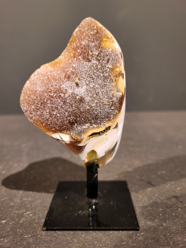 <strong>Agaat op standaard, 0,1kg, 10cm hoog, 7,- euro, nr. 1</strong>

<strong>Beschrijving Agaat.</strong>

Agaat is een veelzijdige edelsteen die bekend staat om zijn prachtige kleurbanden en patronen. Het is een variëteit van het mineraal kwarts, meer specifiek chalcedoon, en wordt vaak gebruikt in sieraden en als decoratieve steen. 
<strong>Algemene kenmerken:</strong>
Agaat is een microkristallijne vorm van kwarts, bestaande uit microscopisch kleine kristallen. 
<strong>Kleuren en patronen:</strong>
Agaat komt voor in vele kleuren, vaak met banden of lagen in verschillende tinten. 
Agaat is een populaire keuze voor het maken van kettingen, armbanden, ringen en andere sieraden vanwege de esthetische aantrekkingskracht en duurzaamheid. 
<strong>Spirituele eigenschappen:</strong>
Agaat wordt vaak geassocieerd met aardende, stabiliserende en beschermende eigenschappen. 
<strong>Helende werking:</strong>
Er wordt aangenomen dat agaat kan helpen bij het verminderen van stress, het bevorderen van emotioneel evenwicht en het versterken van het zelfvertrouwen. 
<strong>Verzorging van agaat:</strong>
Agaat is relatief gemakkelijk te onderhouden. Het kan worden gereinigd met lauw water, de rook van witte salie of palo santo, of door het op een hematiet- of bergkristal-cluster te plaatsen. 

<strong>-	Kunstgalerie-Arnold -</strong>