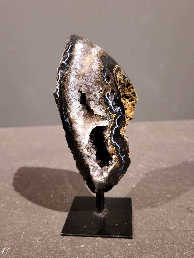 <strong>Agaat op standaard, 0,3kg, 14cm hoog, 17,- euro, nr. 48</strong>

<strong>Beschrijving Agaat.</strong>

Agaat is een veelzijdige edelsteen die bekend staat om zijn prachtige kleurbanden en patronen. Het is een variëteit van het mineraal kwarts, meer specifiek chalcedoon, en wordt vaak gebruikt in sieraden en als decoratieve steen. 
<strong>Algemene kenmerken:</strong>
Agaat is een microkristallijne vorm van kwarts, bestaande uit microscopisch kleine kristallen. 
<strong>Kleuren en patronen:</strong>
Agaat komt voor in vele kleuren, vaak met banden of lagen in verschillende tinten. 
Agaat is een populaire keuze voor het maken van kettingen, armbanden, ringen en andere sieraden vanwege de esthetische aantrekkingskracht en duurzaamheid. 
<strong>Spirituele eigenschappen:</strong>
Agaat wordt vaak geassocieerd met aardende, stabiliserende en beschermende eigenschappen. 
<strong>Helende werking:</strong>
Er wordt aangenomen dat agaat kan helpen bij het verminderen van stress, het bevorderen van emotioneel evenwicht en het versterken van het zelfvertrouwen. 
<strong>Verzorging van agaat:</strong>
Agaat is relatief gemakkelijk te onderhouden. Het kan worden gereinigd met lauw water, de rook van witte salie of palo santo, of door het op een hematiet- of bergkristal-cluster te plaatsen. 

<strong>-	Kunstgalerie-Arnold -</strong>