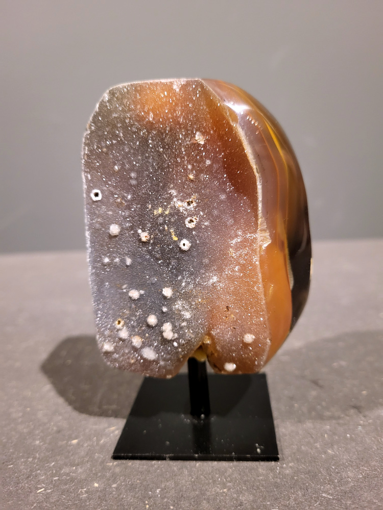 <strong>Agaat op standaard, 0,4kg, 11cm hoog, 18,- euro, nr. 45</strong>

<strong>Beschrijving Agaat.</strong>

Agaat is een veelzijdige edelsteen die bekend staat om zijn prachtige kleurbanden en patronen. Het is een variëteit van het mineraal kwarts, meer specifiek chalcedoon, en wordt vaak gebruikt in sieraden en als decoratieve steen. 
<strong>Algemene kenmerken:</strong>
Agaat is een microkristallijne vorm van kwarts, bestaande uit microscopisch kleine kristallen. 
<strong>Kleuren en patronen:</strong>
Agaat komt voor in vele kleuren, vaak met banden of lagen in verschillende tinten. 
Agaat is een populaire keuze voor het maken van kettingen, armbanden, ringen en andere sieraden vanwege de esthetische aantrekkingskracht en duurzaamheid. 
<strong>Spirituele eigenschappen:</strong>
Agaat wordt vaak geassocieerd met aardende, stabiliserende en beschermende eigenschappen. 
<strong>Helende werking:</strong>
Er wordt aangenomen dat agaat kan helpen bij het verminderen van stress, het bevorderen van emotioneel evenwicht en het versterken van het zelfvertrouwen. 
<strong>Verzorging van agaat:</strong>
Agaat is relatief gemakkelijk te onderhouden. Het kan worden gereinigd met lauw water, de rook van witte salie of palo santo, of door het op een hematiet- of bergkristal-cluster te plaatsen. 

<strong>-	Kunstgalerie-Arnold -</strong>