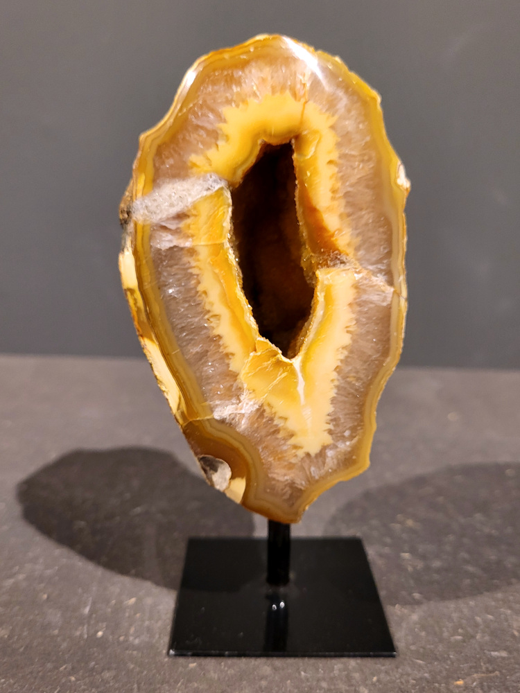 <strong>Agaat op standaard, 0,5kg, 14cm hoog, 26,- euro, nr. 40</strong>

<strong>Beschrijving Agaat.</strong>

Agaat is een veelzijdige edelsteen die bekend staat om zijn prachtige kleurbanden en patronen. Het is een variëteit van het mineraal kwarts, meer specifiek chalcedoon, en wordt vaak gebruikt in sieraden en als decoratieve steen. 
<strong>Algemene kenmerken:</strong>
Agaat is een microkristallijne vorm van kwarts, bestaande uit microscopisch kleine kristallen. 
<strong>Kleuren en patronen:</strong>
Agaat komt voor in vele kleuren, vaak met banden of lagen in verschillende tinten. 
Agaat is een populaire keuze voor het maken van kettingen, armbanden, ringen en andere sieraden vanwege de esthetische aantrekkingskracht en duurzaamheid. 
<strong>Spirituele eigenschappen:</strong>
Agaat wordt vaak geassocieerd met aardende, stabiliserende en beschermende eigenschappen. 
<strong>Helende werking:</strong>
Er wordt aangenomen dat agaat kan helpen bij het verminderen van stress, het bevorderen van emotioneel evenwicht en het versterken van het zelfvertrouwen. 
<strong>Verzorging van agaat:</strong>
Agaat is relatief gemakkelijk te onderhouden. Het kan worden gereinigd met lauw water, de rook van witte salie of palo santo, of door het op een hematiet- of bergkristal-cluster te plaatsen. 

<strong>-	Kunstgalerie-Arnold -</strong>