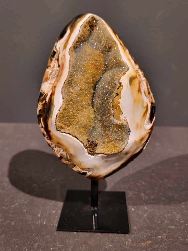 <strong>Agaat op standaard, 0,5kg, 15cm hoog, 27,- euro, nr. 39</strong>

<strong>Beschrijving Agaat.</strong>

Agaat is een veelzijdige edelsteen die bekend staat om zijn prachtige kleurbanden en patronen. Het is een variëteit van het mineraal kwarts, meer specifiek chalcedoon, en wordt vaak gebruikt in sieraden en als decoratieve steen. 
<strong>Algemene kenmerken:</strong>
Agaat is een microkristallijne vorm van kwarts, bestaande uit microscopisch kleine kristallen. 
<strong>Kleuren en patronen:</strong>
Agaat komt voor in vele kleuren, vaak met banden of lagen in verschillende tinten. 
Agaat is een populaire keuze voor het maken van kettingen, armbanden, ringen en andere sieraden vanwege de esthetische aantrekkingskracht en duurzaamheid. 
<strong>Spirituele eigenschappen:</strong>
Agaat wordt vaak geassocieerd met aardende, stabiliserende en beschermende eigenschappen. 
<strong>Helende werking:</strong>
Er wordt aangenomen dat agaat kan helpen bij het verminderen van stress, het bevorderen van emotioneel evenwicht en het versterken van het zelfvertrouwen. 
<strong>Verzorging van agaat:</strong>
Agaat is relatief gemakkelijk te onderhouden. Het kan worden gereinigd met lauw water, de rook van witte salie of palo santo, of door het op een hematiet- of bergkristal-cluster te plaatsen. 

<strong>-	Kunstgalerie-Arnold -</strong>