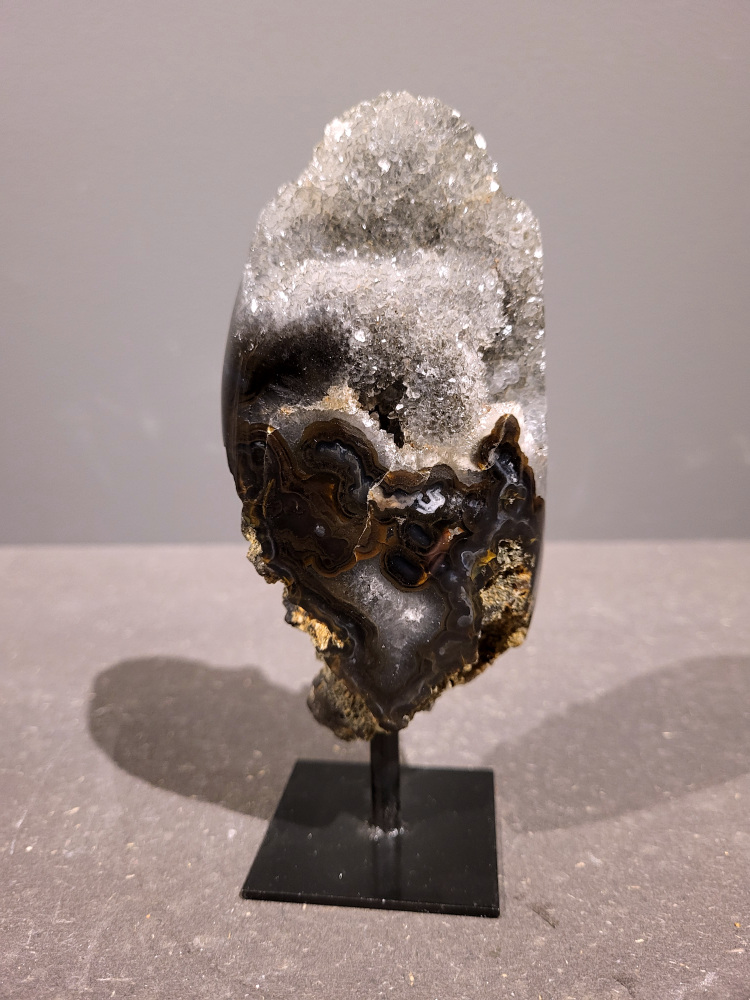 <strong>Agaat op standaard, 0,5kg, 16cm hoog, 23,- euro, nr. 37</strong>

<strong>Beschrijving Agaat.</strong>

Agaat is een veelzijdige edelsteen die bekend staat om zijn prachtige kleurbanden en patronen. Het is een variëteit van het mineraal kwarts, meer specifiek chalcedoon, en wordt vaak gebruikt in sieraden en als decoratieve steen. 
<strong>Algemene kenmerken:</strong>
Agaat is een microkristallijne vorm van kwarts, bestaande uit microscopisch kleine kristallen. 
<strong>Kleuren en patronen:</strong>
Agaat komt voor in vele kleuren, vaak met banden of lagen in verschillende tinten. 
Agaat is een populaire keuze voor het maken van kettingen, armbanden, ringen en andere sieraden vanwege de esthetische aantrekkingskracht en duurzaamheid. 
<strong>Spirituele eigenschappen:</strong>
Agaat wordt vaak geassocieerd met aardende, stabiliserende en beschermende eigenschappen. 
<strong>Helende werking:</strong>
Er wordt aangenomen dat agaat kan helpen bij het verminderen van stress, het bevorderen van emotioneel evenwicht en het versterken van het zelfvertrouwen. 
<strong>Verzorging van agaat:</strong>
Agaat is relatief gemakkelijk te onderhouden. Het kan worden gereinigd met lauw water, de rook van witte salie of palo santo, of door het op een hematiet- of bergkristal-cluster te plaatsen. 

<strong>-	Kunstgalerie-Arnold -</strong>