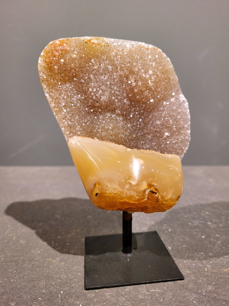 <strong>Agaat op standaard, 0,6kg, 14cm hoog, 28,- euro, nr. 35</strong>

<strong>Beschrijving Agaat.</strong>

Agaat is een veelzijdige edelsteen die bekend staat om zijn prachtige kleurbanden en patronen. Het is een variëteit van het mineraal kwarts, meer specifiek chalcedoon, en wordt vaak gebruikt in sieraden en als decoratieve steen. 
<strong>Algemene kenmerken:</strong>
Agaat is een microkristallijne vorm van kwarts, bestaande uit microscopisch kleine kristallen. 
<strong>Kleuren en patronen:</strong>
Agaat komt voor in vele kleuren, vaak met banden of lagen in verschillende tinten. 
Agaat is een populaire keuze voor het maken van kettingen, armbanden, ringen en andere sieraden vanwege de esthetische aantrekkingskracht en duurzaamheid. 
<strong>Spirituele eigenschappen:</strong>
Agaat wordt vaak geassocieerd met aardende, stabiliserende en beschermende eigenschappen. 
<strong>Helende werking:</strong>
Er wordt aangenomen dat agaat kan helpen bij het verminderen van stress, het bevorderen van emotioneel evenwicht en het versterken van het zelfvertrouwen. 
<strong>Verzorging van agaat:</strong>
Agaat is relatief gemakkelijk te onderhouden. Het kan worden gereinigd met lauw water, de rook van witte salie of palo santo, of door het op een hematiet- of bergkristal-cluster te plaatsen. 

<strong>-	Kunstgalerie-Arnold -</strong>