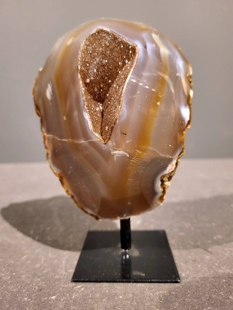 <strong>Agaat op standaard, 0,7 kg, 14cm hoog, 35,- euro, nr. 33</strong>

<strong>Beschrijving Agaat.</strong>

Agaat is een veelzijdige edelsteen die bekend staat om zijn prachtige kleurbanden en patronen. Het is een variëteit van het mineraal kwarts, meer specifiek chalcedoon, en wordt vaak gebruikt in sieraden en als decoratieve steen. 
<strong>Algemene kenmerken:</strong>
Agaat is een microkristallijne vorm van kwarts, bestaande uit microscopisch kleine kristallen. 
<strong>Kleuren en patronen:</strong>
Agaat komt voor in vele kleuren, vaak met banden of lagen in verschillende tinten. 
Agaat is een populaire keuze voor het maken van kettingen, armbanden, ringen en andere sieraden vanwege de esthetische aantrekkingskracht en duurzaamheid. 
<strong>Spirituele eigenschappen:</strong>
Agaat wordt vaak geassocieerd met aardende, stabiliserende en beschermende eigenschappen. 
<strong>Helende werking:</strong>
Er wordt aangenomen dat agaat kan helpen bij het verminderen van stress, het bevorderen van emotioneel evenwicht en het versterken van het zelfvertrouwen. 
<strong>Verzorging van agaat:</strong>
Agaat is relatief gemakkelijk te onderhouden. Het kan worden gereinigd met lauw water, de rook van witte salie of palo santo, of door het op een hematiet- of bergkristal-cluster te plaatsen. 

<strong>-	Kunstgalerie-Arnold -</strong>