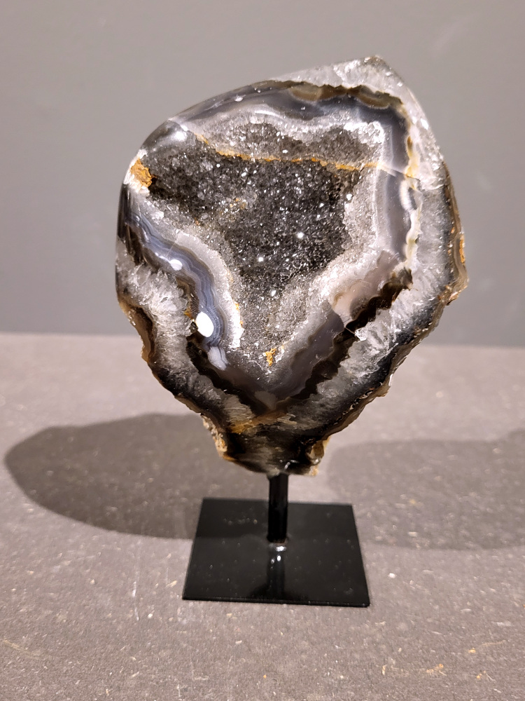 <strong>Agaat op standaard, 0,7 kg, 15cm hoog, 36,- euro, nr. 8</strong>

<strong>Beschrijving Agaat.</strong>

Agaat is een veelzijdige edelsteen die bekend staat om zijn prachtige kleurbanden en patronen. Het is een variëteit van het mineraal kwarts, meer specifiek chalcedoon, en wordt vaak gebruikt in sieraden en als decoratieve steen. 
<strong>Algemene kenmerken:</strong>
Agaat is een microkristallijne vorm van kwarts, bestaande uit microscopisch kleine kristallen. 
<strong>Kleuren en patronen:</strong>
Agaat komt voor in vele kleuren, vaak met banden of lagen in verschillende tinten. 
Agaat is een populaire keuze voor het maken van kettingen, armbanden, ringen en andere sieraden vanwege de esthetische aantrekkingskracht en duurzaamheid. 
<strong>Spirituele eigenschappen:</strong>
Agaat wordt vaak geassocieerd met aardende, stabiliserende en beschermende eigenschappen. 
<strong>Helende werking:</strong>
Er wordt aangenomen dat agaat kan helpen bij het verminderen van stress, het bevorderen van emotioneel evenwicht en het versterken van het zelfvertrouwen. 
<strong>Verzorging van agaat:</strong>
Agaat is relatief gemakkelijk te onderhouden. Het kan worden gereinigd met lauw water, de rook van witte salie of palo santo, of door het op een hematiet- of bergkristal-cluster te plaatsen. 

<strong>-	Kunstgalerie-Arnold -</strong>