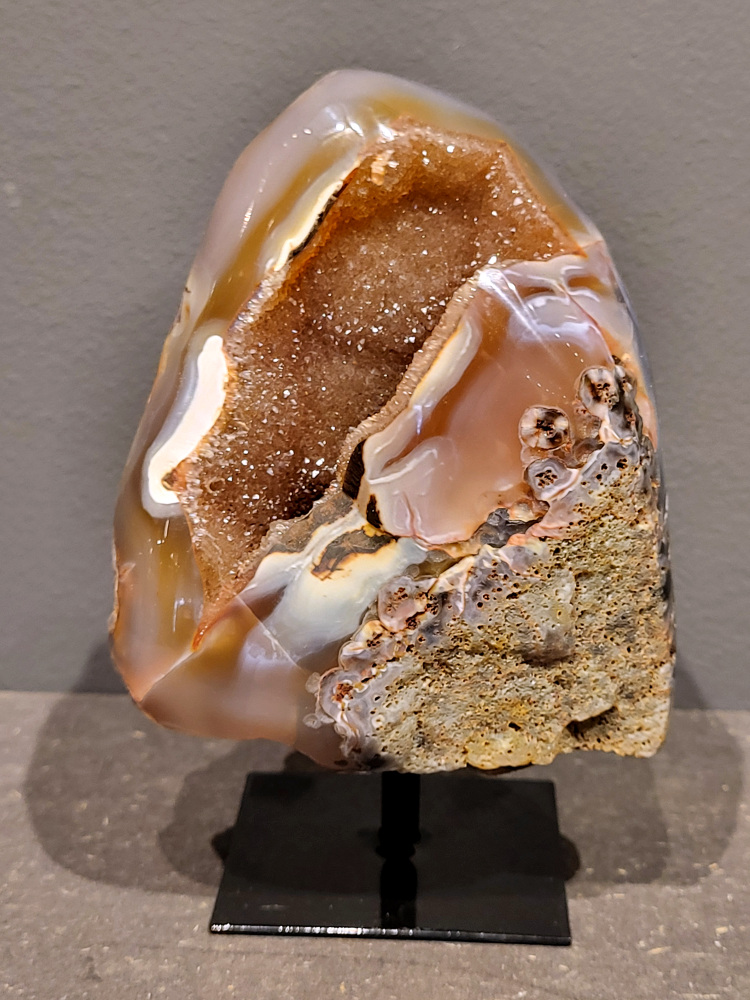 <strong>Agaat op standaard, 14cm hoog, 0,6kg, 28,- euro, nr. 10 </strong>

Agaat is een veelzijdige edelsteen die bekend staat om zijn prachtige kleurbanden en patronen. Het is een variëteit van het mineraal kwarts, meer specifiek chalcedoon, en wordt vaak gebruikt in sieraden en als decoratieve steen. 
<strong>Algemene kenmerken:</strong>
Agaat is een microkristallijne vorm van kwarts, bestaande uit microscopisch kleine kristallen. 
<strong>Kleuren en patronen:</strong>
Agaat komt voor in vele kleuren, vaak met banden of lagen in verschillende tinten. 
Agaat is een populaire keuze voor het maken van kettingen, armbanden, ringen en andere sieraden vanwege de esthetische aantrekkingskracht en duurzaamheid. 
<strong>Spirituele eigenschappen:</strong>
Agaat wordt vaak geassocieerd met aardende, stabiliserende en beschermende eigenschappen. 
<strong>Helende werking:</strong>
Er wordt aangenomen dat agaat kan helpen bij het verminderen van stress, het bevorderen van emotioneel evenwicht en het versterken van het zelfvertrouwen. 
Verzorging van agaat:
Agaat is relatief gemakkelijk te onderhouden. Het kan worden gereinigd met lauw water, de rook van witte salie of palo santo, of door het op een hematiet- of bergkristal-cluster te plaatsen. 

<strong>-	Kunstgalerie-Arnold -</strong>