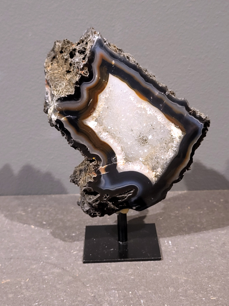 <strong>Agaat op standaard, 15cm hoog, 0,5 kg, 23,- euro, nr. 26</strong>

Beschrijving Agaat.

Agaat is een veelzijdige edelsteen die bekend staat om zijn prachtige kleurbanden en patronen. Het is een variëteit van het mineraal kwarts, meer specifiek chalcedoon, en wordt vaak gebruikt in sieraden en als decoratieve steen. 
<strong>Algemene kenmerken:</strong>
Agaat is een microkristallijne vorm van kwarts, bestaande uit microscopisch kleine kristallen. 
<strong>Kleuren en patronen:</strong>
Agaat komt voor in vele kleuren, vaak met banden of lagen in verschillende tinten. 
Agaat is een populaire keuze voor het maken van kettingen, armbanden, ringen en andere sieraden vanwege de esthetische aantrekkingskracht en duurzaamheid. 
<strong>Spirituele eigenschappen:</strong>
Agaat wordt vaak geassocieerd met aardende, stabiliserende en beschermende eigenschappen. 
<strong>Helende werking:</strong>
Er wordt aangenomen dat agaat kan helpen bij het verminderen van stress, het bevorderen van emotioneel evenwicht en het versterken van het zelfvertrouwen. 
<strong>Verzorging van agaat:</strong>
Agaat is relatief gemakkelijk te onderhouden. Het kan worden gereinigd met lauw water, de rook van witte salie of palo santo, of door het op een hematiet- of bergkristal-cluster te plaatsen. 

<strong>-	Kunstgalerie-Arnold -</strong>