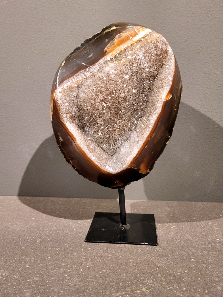 <strong>Agaat op standaard, 1,5kg, 22cm hoog, 74,- euro, nr. 27</strong>

<strong>Beschrijving Agaat.</strong>

Agaat is een veelzijdige edelsteen die bekend staat om zijn prachtige kleurbanden en patronen. Het is een variëteit van het mineraal kwarts, meer specifiek chalcedoon, en wordt vaak gebruikt in sieraden en als decoratieve steen. 
<strong>Algemene kenmerken:</strong>
Agaat is een microkristallijne vorm van kwarts, bestaande uit microscopisch kleine kristallen. 
<strong>Kleuren en patronen:</strong>
Agaat komt voor in vele kleuren, vaak met banden of lagen in verschillende tinten. 
Agaat is een populaire keuze voor het maken van kettingen, armbanden, ringen en andere sieraden vanwege de esthetische aantrekkingskracht en duurzaamheid. 
<strong>Spirituele eigenschappen:</strong>
Agaat wordt vaak geassocieerd met aardende, stabiliserende en beschermende eigenschappen. 
<strong>Helende werking:</strong>
Er wordt aangenomen dat agaat kan helpen bij het verminderen van stress, het bevorderen van emotioneel evenwicht en het versterken van het zelfvertrouwen. 
<strong>Verzorging van agaat:</strong>
Agaat is relatief gemakkelijk te onderhouden. Het kan worden gereinigd met lauw water, de rook van witte salie of palo santo, of door het op een hematiet- of bergkristal-cluster te plaatsen. 

<strong>-	Kunstgalerie-Arnold -</strong>