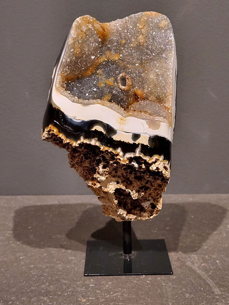 <strong>Agaat op standaard, 18cm hoog, 0,9 kg, 44,- euro, nr. 23</strong>

Agaat is een veelzijdige edelsteen die bekend staat om zijn prachtige kleurbanden en patronen. Het is een variëteit van het mineraal kwarts, meer specifiek chalcedoon, en wordt vaak gebruikt in sieraden en als decoratieve steen. 
<strong>Algemene kenmerken:</strong>
Agaat is een microkristallijne vorm van kwarts, bestaande uit microscopisch kleine kristallen. 
<strong>Kleuren en patronen:</strong>
Agaat komt voor in vele kleuren, vaak met banden of lagen in verschillende tinten. 
Agaat is een populaire keuze voor het maken van kettingen, armbanden, ringen en andere sieraden vanwege de esthetische aantrekkingskracht en duurzaamheid. 
<strong>Spirituele eigenschappen:</strong>
Agaat wordt vaak geassocieerd met aardende, stabiliserende en beschermende eigenschappen. 
<strong>Helende werking:</strong>
Er wordt aangenomen dat agaat kan helpen bij het verminderen van stress, het bevorderen van emotioneel evenwicht en het versterken van het zelfvertrouwen. 
<strong>Verzorging van agaat:</strong>
Agaat is relatief gemakkelijk te onderhouden. Het kan worden gereinigd met lauw water, de rook van witte salie of palo santo, of door het op een hematiet- of bergkristal-cluster te plaatsen. 

<strong>-	Kunstgalerie-Arnold -</strong>