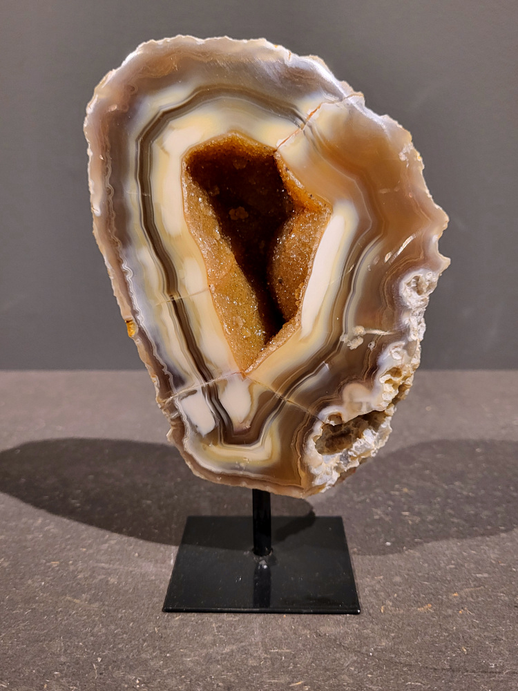 <strong>Agaat op standaard, 1kg, 17cm hoog, 49,- euro, nr. 9</strong>

<strong>Beschrijving Agaat.</strong>

Agaat is een veelzijdige edelsteen die bekend staat om zijn prachtige kleurbanden en patronen. Het is een variëteit van het mineraal kwarts, meer specifiek chalcedoon, en wordt vaak gebruikt in sieraden en als decoratieve steen. 
<strong>Algemene kenmerken:</strong>
Agaat is een microkristallijne vorm van kwarts, bestaande uit microscopisch kleine kristallen. 
<strong>Kleuren en patronen:</strong>
Agaat komt voor in vele kleuren, vaak met banden of lagen in verschillende tinten. 
Agaat is een populaire keuze voor het maken van kettingen, armbanden, ringen en andere sieraden vanwege de esthetische aantrekkingskracht en duurzaamheid. 
<strong>Spirituele eigenschappen:</strong>
Agaat wordt vaak geassocieerd met aardende, stabiliserende en beschermende eigenschappen. 
<strong>Helende werking:</strong>
Er wordt aangenomen dat agaat kan helpen bij het verminderen van stress, het bevorderen van emotioneel evenwicht en het versterken van het zelfvertrouwen. 
<strong>Verzorging van agaat:</strong>
Agaat is relatief gemakkelijk te onderhouden. Het kan worden gereinigd met lauw water, de rook van witte salie of palo santo, of door het op een hematiet- of bergkristal-cluster te plaatsen. 

<strong>-	Kunstgalerie-Arnold -</strong>