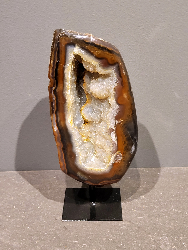 <strong>Agaat op standaard, 20cm hoog, 1,1 kg, 53,- euro, nr. 24</strong>

Beschrijving Agaat.

Agaat is een veelzijdige edelsteen die bekend staat om zijn prachtige kleurbanden en patronen. Het is een variëteit van het mineraal kwarts, meer specifiek chalcedoon, en wordt vaak gebruikt in sieraden en als decoratieve steen. 
<strong>Algemene kenmerken:</strong>
Agaat is een microkristallijne vorm van kwarts, bestaande uit microscopisch kleine kristallen. 
<strong>Kleuren en patronen:</strong>
Agaat komt voor in vele kleuren, vaak met banden of lagen in verschillende tinten. 
Agaat is een populaire keuze voor het maken van kettingen, armbanden, ringen en andere sieraden vanwege de esthetische aantrekkingskracht en duurzaamheid. 
<strong>Spirituele eigenschappen:</strong>
Agaat wordt vaak geassocieerd met aardende, stabiliserende en beschermende eigenschappen. 
<strong>Helende werking:</strong>
Er wordt aangenomen dat agaat kan helpen bij het verminderen van stress, het bevorderen van emotioneel evenwicht en het versterken van het zelfvertrouwen. 
<strong>Verzorging van agaat:</strong>
Agaat is relatief gemakkelijk te onderhouden. Het kan worden gereinigd met lauw water, de rook van witte salie of palo santo, of door het op een hematiet- of bergkristal-cluster te plaatsen. 

<strong>-	Kunstgalerie-Arnold -</strong>