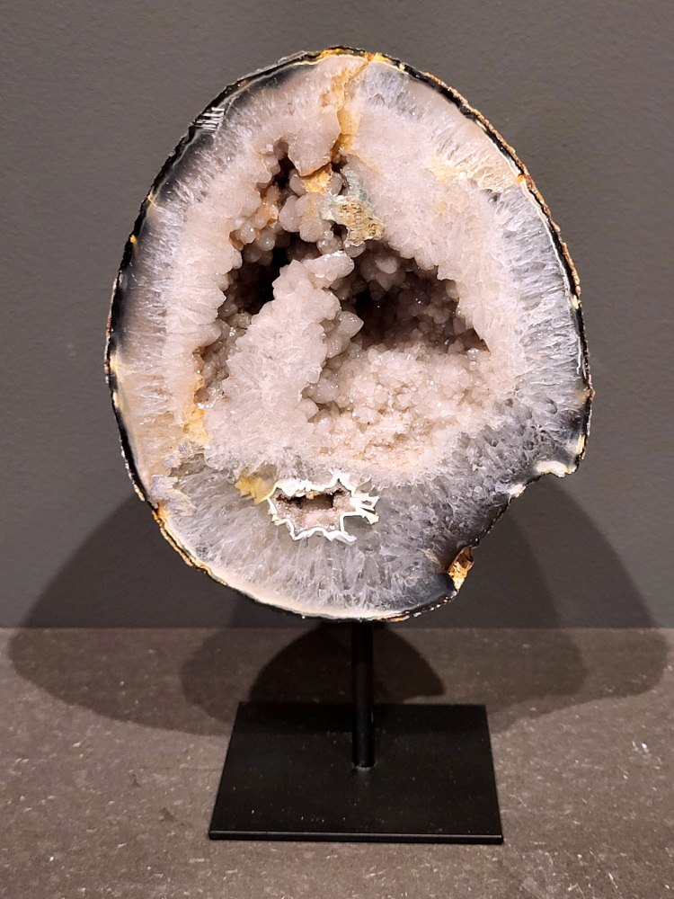 <strong>Agaat op standaard, 20cm hoog, 1,3kg, 66,- euro, nr. 21</strong>

Agaat is een veelzijdige edelsteen die bekend staat om zijn prachtige kleurbanden en patronen. Het is een variëteit van het mineraal kwarts, meer specifiek chalcedoon, en wordt vaak gebruikt in sieraden en als decoratieve steen. 
<strong>Algemene kenmerken:</strong>
Agaat is een microkristallijne vorm van kwarts, bestaande uit microscopisch kleine kristallen. 
<strong>Kleuren en patronen:</strong>
Agaat komt voor in vele kleuren, vaak met banden of lagen in verschillende tinten. 
Agaat is een populaire keuze voor het maken van kettingen, armbanden, ringen en andere sieraden vanwege de esthetische aantrekkingskracht en duurzaamheid. 
<strong>Spirituele eigenschappen:</strong>
Agaat wordt vaak geassocieerd met aardende, stabiliserende en beschermende eigenschappen. 
<strong>Helende werking:</strong>
Er wordt aangenomen dat agaat kan helpen bij het verminderen van stress, het bevorderen van emotioneel evenwicht en het versterken van het zelfvertrouwen. 
<strong>Verzorging van agaat:</strong>
Agaat is relatief gemakkelijk te onderhouden. Het kan worden gereinigd met lauw water, de rook van witte salie of palo santo, of door het op een hematiet- of bergkristal-cluster te plaatsen. 

<strong>-	Kunstgalerie-Arnold -</strong>