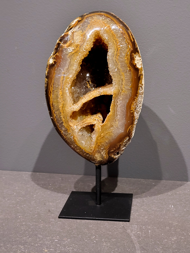 <strong>Agaat op standaard, 23cm hoog, 1,7 kg, 83,- euro, nr. 16</strong>

Agaat is een veelzijdige edelsteen die bekend staat om zijn prachtige kleurbanden en patronen. Het is een variëteit van het mineraal kwarts, meer specifiek chalcedoon, en wordt vaak gebruikt in sieraden en als decoratieve steen. 
<strong>Algemene kenmerken:</strong>
Agaat is een microkristallijne vorm van kwarts, bestaande uit microscopisch kleine kristallen. 
<strong>Kleuren en patronen:</strong>
Agaat komt voor in vele kleuren, vaak met banden of lagen in verschillende tinten. 
Agaat is een populaire keuze voor het maken van kettingen, armbanden, ringen en andere sieraden vanwege de esthetische aantrekkingskracht en duurzaamheid. 
<strong>Spirituele eigenschappen:</strong>
Agaat wordt vaak geassocieerd met aardende, stabiliserende en beschermende eigenschappen. 
<strong>Helende werking:</strong>
Er wordt aangenomen dat agaat kan helpen bij het verminderen van stress, het bevorderen van emotioneel evenwicht en het versterken van het zelfvertrouwen. 
<strong>Verzorging van agaat:</strong>
Agaat is relatief gemakkelijk te onderhouden. Het kan worden gereinigd met lauw water, de rook van witte salie of palo santo, of door het op een hematiet- of bergkristal-cluster te plaatsen. 

<strong>-	Kunstgalerie-Arnold -</strong>