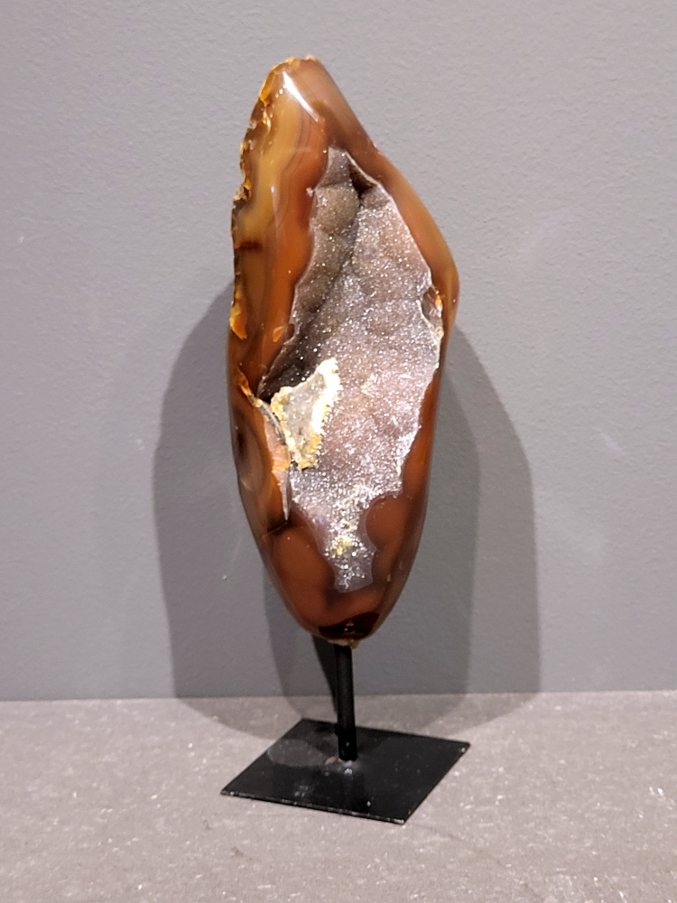 <strong>Agaat op standaard, 25cm hoog, 0,8 kg, 40,- euro, nr. 14</strong>

Agaat is een veelzijdige edelsteen die bekend staat om zijn prachtige kleurbanden en patronen. Het is een variëteit van het mineraal kwarts, meer specifiek chalcedoon, en wordt vaak gebruikt in sieraden en als decoratieve steen. 
<strong>Algemene kenmerken:</strong>
Agaat is een microkristallijne vorm van kwarts, bestaande uit microscopisch kleine kristallen. 
<strong>Kleuren en patronen:</strong>
Agaat komt voor in vele kleuren, vaak met banden of lagen in verschillende tinten. 
Agaat is een populaire keuze voor het maken van kettingen, armbanden, ringen en andere sieraden vanwege de esthetische aantrekkingskracht en duurzaamheid. 
<strong>Spirituele eigenschappen:</strong>
Agaat wordt vaak geassocieerd met aardende, stabiliserende en beschermende eigenschappen. 
<strong>Helende werking:</strong>
Er wordt aangenomen dat agaat kan helpen bij het verminderen van stress, het bevorderen van emotioneel evenwicht en het versterken van het zelfvertrouwen. 
<strong>Verzorging van agaat:</strong>
Agaat is relatief gemakkelijk te onderhouden. Het kan worden gereinigd met lauw water, de rook van witte salie of palo santo, of door het op een hematiet- of bergkristal-cluster te plaatsen. 

<strong>-	Kunstgalerie-Arnold -</strong>