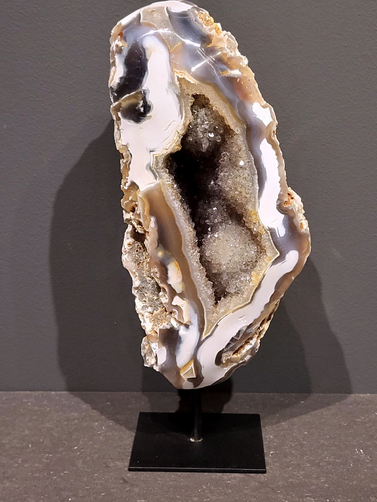 <strong>Agaat op standaard, 26cm hoog, 1,7kg, 86,- euro, nr. 11</strong>

Agaat is een veelzijdige edelsteen die bekend staat om zijn prachtige kleurbanden en patronen. Het is een variëteit van het mineraal kwarts, meer specifiek chalcedoon, en wordt vaak gebruikt in sieraden en als decoratieve steen. 
<strong>Algemene kenmerken:</strong>
Agaat is een microkristallijne vorm van kwarts, bestaande uit microscopisch kleine kristallen. 
<strong>Kleuren en patronen:
Agaat komt voor in ve</strong>le kleuren, vaak met banden of lagen in verschillende tinten. 
Agaat is een populaire keuze voor het maken van kettingen, armbanden, ringen en andere sieraden vanwege de esthetische aantrekkingskracht en duurzaamheid. 
<strong>Spirituele eigenschappen:</strong>
Agaat wordt vaak geassocieerd met aardende, stabiliserende en beschermende eigenschappen. 
<strong>Helende werking:</strong>
Er wordt aangenomen dat agaat kan helpen bij het verminderen van stress, het bevorderen van emotioneel evenwicht en het versterken van het zelfvertrouwen. 
<strong>Verzorging van agaat:</strong>
Agaat is relatief gemakkelijk te onderhouden. Het kan worden gereinigd met lauw water, de rook van witte salie of palo santo, of door het op een hematiet- of bergkristal-cluster te plaatsen. 

<strong>-	Kunstgalerie-Arnold -</strong>