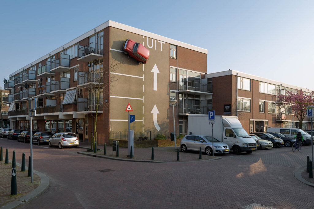 <strong>Laar, Theo van Laar, is geboren in 1943 in Den Haag. nr. 26</strong>Hij was een vrijzinnig kunstenaar die zijn eigen richting bepaalde. <strong>Over het algemeen schilderde hij in een hyperrealistische stijl, die we terug vinden in zijn tekeningen en schilderijen.</strong>
Hij schilderde hoofdzakelijk vanuit de Haagse Schilderswijk en maakte ook als kunstenaar van diverse objecten, <strong>waarvan Het Otootje een belangrijk kunstwerk werd, </strong>wat de buurtbewoners niet wilden missen in hun buurt.
Het kunstwerk was beroemd in de Schilderswijk en werd vrijwel zonder uitzondering zeer gewaardeerd door de buurtbewoners. Maar de ‘Auto tegen de gevel’ uit 1980 van Theo van Laar moest in juli 1996 het veld ruimen. Van de rode Mini viel bij slecht weer een wieldop af, totaal doorgeroest. Binnen een paar dagen werd het vehikel naar beneden getakeld. Jammer, maar het complete kunstwerk zou later dat jaar met de sloop van het gebouw in de De Heemstraat, waaraan het was bevestigd, toch verdwijnen.
<strong>De bewoners van de Haagse Schilderswijk lieten het er niet bij zitten.</strong> Ze voerden succesvol actie. Het duurde een paar jaar voordat een geschikte locatie werd gevonden. In 2004 keerde de Mini terug in de wijk. <strong>De auto draait weer netjes het parkeervak in dat dit keer is geschilderd op een blinde muur van een flat in de Westenbergstraat.</strong> Aangezien deze muur kleiner is dan de muur op de oude locatie, is er een nieuw ontwerp voor de parkeerplaats gemaakt. De parkeervakken staan nu links in plaats van rechts. UIT is naar boven ofwel rechtdoor en niet langer linksaf. Ook is er minder parkeerruimte beschikbaar.