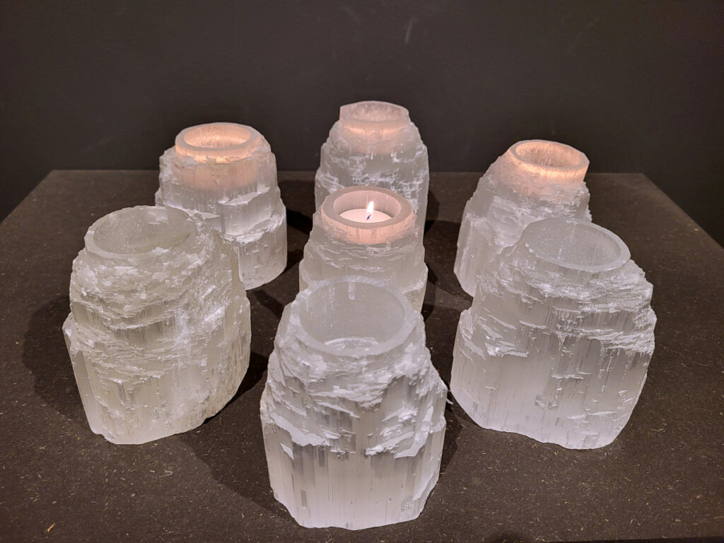 Seleniet, Waxine lichten, 11cm hoog, doorsnee 9 cm, 10,- euro, nr. 5

Seleniet is een vorm van gips, een mineraal met een vezelige structuur. Het staat bekend om zijn heldere, witte kleur en wordt vaak "satijnspaat" genoemd vanwege zijn glans. Seleniet kan ook andere kleuren hebben, zoals geel, oranje en rood. De naam "seleniet" komt van de Griekse maangodin Selene, vanwege de maanachtige glans van de steen.
Eigenschappen en kenmerken:
Kleur: Meestal wit, maar kan ook geel, oranje, rood, groen of blauw zijn.
Vorm: Vaak in lange, dunne kristallen, soms ook als woestijnrozen.
Textuur: Vezelig en glanzend, met een satijnachtige uitstraling.
Hardheid: 2 op de schaal van Mohs, wat betekent dat het zacht is en makkelijk kan krassen.
Vorming: Ontstaat door de verdamping van zoutwatermeren en -zeeën.
Spirituele en helende eigenschappen:
Seleniet wordt vaak gebruikt in spirituele praktijken en meditatie, vanwege de vermeende kalmerende en reinigende werking.
Het wordt vaak geassocieerd met het reinigen en opladen van andere edelstenen.
Seleniet zou helpen om negatieve energie te verwijderen, helderheid van geest te bevorderen en contact te maken met hogere bewustzijnsniveaus.
In de edelsteentherapie wordt seleniet gebruikt voor ontspanning en het loslaten van spanningen.
Toepassingen:
Decoratieve doeleinden, zoals beeldjes en lampen.
Spirituele doeleinden, zoals meditatie en healing.
Sieraden.
Het maken van raampjes (Mariaglas).
Belangrijk: Seleniet is gevoelig voor water en kan oplossen of beschadigen als het te lang met water in aanraking komt.
Andere namen:
Satijnspaat, Mariaglas (heldere variant), Maansteen (soms).