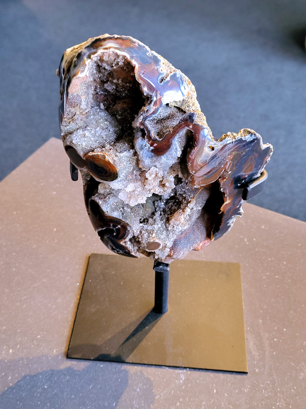 <strong>Agaat op standaard, 2,1 kg, 103,- euro, nr. 53</strong>

<strong>Agaat is een veelzijdige edelsteen die bekend staat om zijn prachtige kleurbanden en patronen.</strong> Het is een variëteit van het mineraal kwarts, meer specifiek chalcedoon, en wordt vaak gebruikt in sieraden en als decoratieve steen. 
<strong>Algemene kenmerken:</strong>
Agaat is een microkristallijne vorm van kwarts, bestaande uit microscopisch kleine kristallen. 
<strong>Kleuren en patronen:</strong>
Agaat komt voor in vele kleuren, vaak met banden of lagen in verschillende tinten. 
Agaat is een populaire keuze voor het maken van kettingen, armbanden, ringen en andere sieraden vanwege de esthetische aantrekkingskracht en duurzaamheid. 
<strong>Spirituele eigenschappen:</strong>
Agaat wordt vaak geassocieerd met aardende, stabiliserende en beschermende eigenschappen. 
<strong>Helende werking:</strong>
Er wordt aangenomen dat agaat kan helpen bij het verminderen van stress, het bevorderen van emotioneel evenwicht en het versterken van het zelfvertrouwen. 
<strong>Verzorging van agaat:</strong>
Agaat is relatief gemakkelijk te onderhouden. Het kan worden gereinigd met lauw water, de rook van witte salie of palo santo, of door het op een hematiet- of bergkristal-cluster te plaatsen.