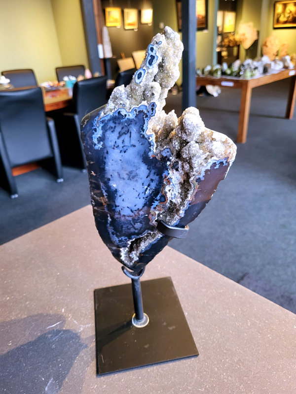 <strong>Agaat op standaard, 4,8kg, 239,- euro, nr. 56</strong>

<strong>Agaat is een veelzijdige edelsteen die bekend staat om zijn prachtige kleurbanden en patronen.</strong> Het is een variëteit van het mineraal kwarts, meer specifiek chalcedoon, en wordt vaak gebruikt in sieraden en als decoratieve steen. 
<strong>Algemene kenmerken:</strong>
Agaat is een microkristallijne vorm van kwarts, bestaande uit microscopisch kleine kristallen. 
<strong>Kleuren en patronen:</strong>
Agaat komt voor in vele kleuren, vaak met banden of lagen in verschillende tinten. 
Agaat is een populaire keuze voor het maken van kettingen, armbanden, ringen en andere sieraden vanwege de esthetische aantrekkingskracht en duurzaamheid. 
<strong>Spirituele eigenschappen:</strong>
Agaat wordt vaak geassocieerd met aardende, stabiliserende en beschermende eigenschappen. 
<strong>Helende werking:</strong>
Er wordt aangenomen dat agaat kan helpen bij het verminderen van stress, het bevorderen van emotioneel evenwicht en het versterken van het zelfvertrouwen. 
<strong>Verzorging van agaat:</strong>
Agaat is relatief gemakkelijk te onderhouden. Het kan worden gereinigd met lauw water, de rook van witte salie of palo santo, of door het op een hematiet- of bergkristal-cluster te plaatsen.