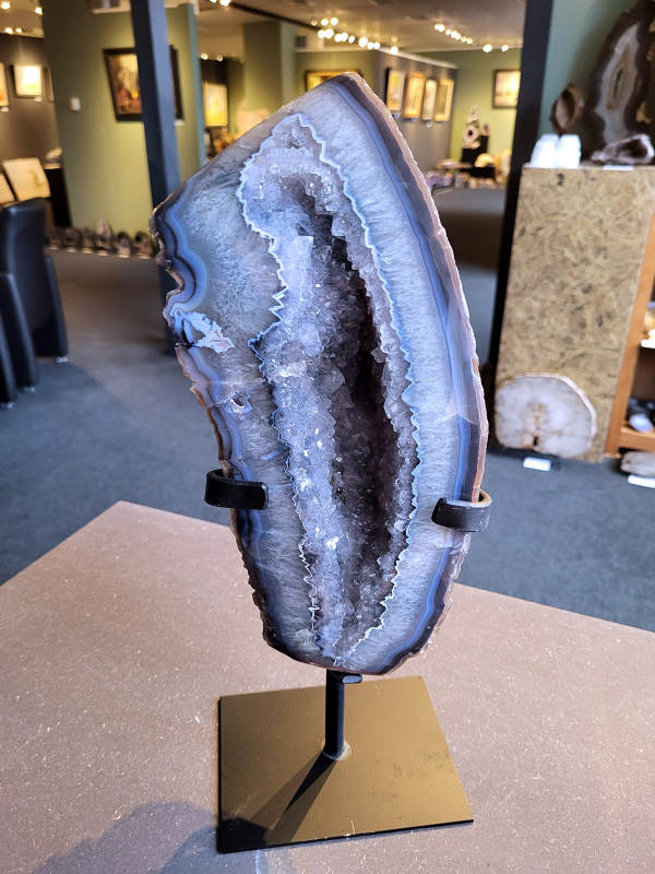 <strong>Agaat op standaard, 6,9 kg, 344,- euro, nr. 57</strong>

<strong>Agaat is een veelzijdige edelsteen die bekend staat om zijn prachtige kleurbanden en patronen.</strong> Het is een variëteit van het mineraal kwarts, meer specifiek chalcedoon, en wordt vaak gebruikt in sieraden en als decoratieve steen. 
<strong>Algemene kenmerken:</strong>
Agaat is een microkristallijne vorm van kwarts, bestaande uit microscopisch kleine kristallen. 
<strong>Kleuren en patronen:</strong>
Agaat komt voor in vele kleuren, vaak met banden of lagen in verschillende tinten. 
Agaat is een populaire keuze voor het maken van kettingen, armbanden, ringen en andere sieraden vanwege de esthetische aantrekkingskracht en duurzaamheid. 
<strong>Spirituele eigenschappen:</strong>
Agaat wordt vaak geassocieerd met aardende, stabiliserende en beschermende eigenschappen. 
<strong>Helende werking:</strong>
Er wordt aangenomen dat agaat kan helpen bij het verminderen van stress, het bevorderen van emotioneel evenwicht en het versterken van het zelfvertrouwen. 
<strong>Verzorging van agaat:</strong>
Agaat is relatief gemakkelijk te onderhouden. Het kan worden gereinigd met lauw water, de rook van witte salie of palo santo, of door het op een hematiet- of bergkristal-cluster te plaatsen.