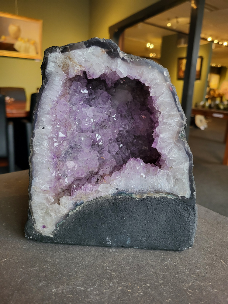 Amethist, Amethist Geode, Kunstgalerie Arnold, 3,4 kg, 34,- euro, nr. 6

Beschrijving Amethist.
Amethist is een paarse variëteit van kwarts, bekend om zijn kalmerende en spirituele eigenschappen. De kleur varieert van licht lila tot diep violet en wordt veroorzaakt door sporen van ijzer en andere elementen. Amethist wordt al eeuwenlang gewaardeerd, zowel vanwege zijn esthetische schoonheid als zijn vermeende genezende en beschermende krachten. 
Amethist is een kwartskristal, vaak te vinden in geodes (holtes in gesteente) of als afzonderlijke kristallen. 
De kleur varieert van lichtpaars tot diep violet, soms met roze of blauwe tinten. 
De kleurintensiteit kan variëren, waarbij donkerdere amethisten vaak als kwalitatief worden beschouwd. 
Soms vertoont amethist dichroïsme, waarbij je verschillende kleuren kunt zien wanneer je de steen in het licht draait. 

Vindplaatsen:
Amethist wordt gevonden in verschillende delen van de wereld, waaronder Brazilië, Uruguay, Zambia, Madagaskar, Rusland en Canada.
Het wordt vaak gevonden in bergachtige gebieden. 

Gebruik:
Amethist wordt gebruikt in sieraden, decoratieve objecten en als helende steen. 
Het wordt vaak gedragen als hanger, ring of armband, of geplaatst in ruimtes om de energie te zuiveren. 
Amethist wordt ook gebruikt in meditatie en andere spirituele praktijken. 
