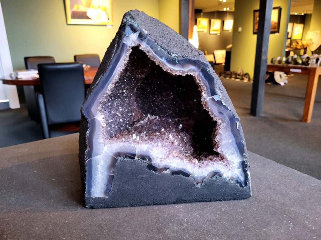 Amethist, Amethist Geode, Kunstgalerie Arnold, 8,6 kg, 86,- euro, nr. 9

Beschrijving Amethist.
Amethist is een paarse variëteit van kwarts, bekend om zijn kalmerende en spirituele eigenschappen. De kleur varieert van licht lila tot diep violet en wordt veroorzaakt door sporen van ijzer en andere elementen. Amethist wordt al eeuwenlang gewaardeerd, zowel vanwege zijn esthetische schoonheid als zijn vermeende genezende en beschermende krachten. 
Amethist is een kwartskristal, vaak te vinden in geodes (holtes in gesteente) of als afzonderlijke kristallen. 
De kleur varieert van lichtpaars tot diep violet, soms met roze of blauwe tinten. 
De kleurintensiteit kan variëren, waarbij donkerdere amethisten vaak als kwalitatief worden beschouwd. 
Soms vertoont amethist dichroïsme, waarbij je verschillende kleuren kunt zien wanneer je de steen in het licht draait. 

Vindplaatsen:
Amethist wordt gevonden in verschillende delen van de wereld, waaronder Brazilië, Uruguay, Zambia, Madagaskar, Rusland en Canada.
Het wordt vaak gevonden in bergachtige gebieden. 

Gebruik:
Amethist wordt gebruikt in sieraden, decoratieve objecten en als helende steen. 
Het wordt vaak gedragen als hanger, ring of armband, of geplaatst in ruimtes om de energie te zuiveren. 
Amethist wordt ook gebruikt in meditatie en andere spirituele praktijken. 
