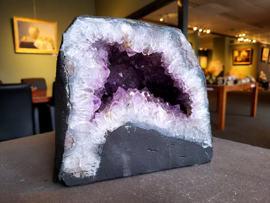 Amethist, Amethist Geode, Kunstgalerie Arnold, 9 kg, 95,- euro, nr. 10

Beschrijving Amethist.
Amethist is een paarse variëteit van kwarts, bekend om zijn kalmerende en spirituele eigenschappen. De kleur varieert van licht lila tot diep violet en wordt veroorzaakt door sporen van ijzer en andere elementen. Amethist wordt al eeuwenlang gewaardeerd, zowel vanwege zijn esthetische schoonheid als zijn vermeende genezende en beschermende krachten. 
Amethist is een kwartskristal, vaak te vinden in geodes (holtes in gesteente) of als afzonderlijke kristallen. 
De kleur varieert van lichtpaars tot diep violet, soms met roze of blauwe tinten. 
De kleurintensiteit kan variëren, waarbij donkerdere amethisten vaak als kwalitatief worden beschouwd. 
Soms vertoont amethist dichroïsme, waarbij je verschillende kleuren kunt zien wanneer je de steen in het licht draait. 

Vindplaatsen:
Amethist wordt gevonden in verschillende delen van de wereld, waaronder Brazilië, Uruguay, Zambia, Madagaskar, Rusland en Canada.
Het wordt vaak gevonden in bergachtige gebieden. 

Gebruik:
Amethist wordt gebruikt in sieraden, decoratieve objecten en als helende steen. 
Het wordt vaak gedragen als hanger, ring of armband, of geplaatst in ruimtes om de energie te zuiveren. 
Amethist wordt ook gebruikt in meditatie en andere spirituele praktijken. 
