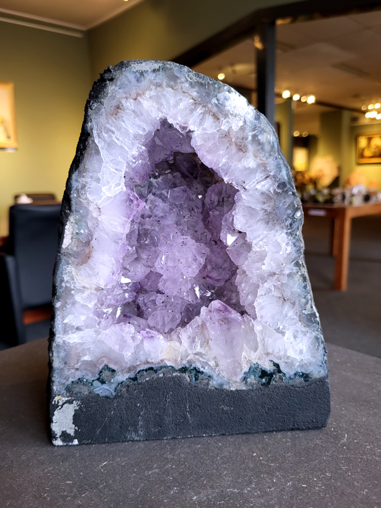 Amethist, Amethist geode met standvlak, 3,8 kg, 38,- euro, Kunstgalerie Arnold, nr. 7

Beschrijving Amethist.
Amethist is een paarse variëteit van kwarts, bekend om zijn kalmerende en spirituele eigenschappen. De kleur varieert van licht lila tot diep violet en wordt veroorzaakt door sporen van ijzer en andere elementen. Amethist wordt al eeuwenlang gewaardeerd, zowel vanwege zijn esthetische schoonheid als zijn vermeende genezende en beschermende krachten. 
Amethist is een kwartskristal, vaak te vinden in geodes (holtes in gesteente) of als afzonderlijke kristallen. 
De kleur varieert van lichtpaars tot diep violet, soms met roze of blauwe tinten. 
De kleurintensiteit kan variëren, waarbij donkerdere amethisten vaak als kwalitatief worden beschouwd. 
Soms vertoont amethist dichroïsme, waarbij je verschillende kleuren kunt zien wanneer je de steen in het licht draait. 

Vindplaatsen:
Amethist wordt gevonden in verschillende delen van de wereld, waaronder Brazilië, Uruguay, Zambia, Madagaskar, Rusland en Canada.
Het wordt vaak gevonden in bergachtige gebieden. 

Gebruik:
Amethist wordt gebruikt in sieraden, decoratieve objecten en als helende steen. 
Het wordt vaak gedragen als hanger, ring of armband, of geplaatst in ruimtes om de energie te zuiveren. 
Amethist wordt ook gebruikt in meditatie en andere spirituele praktijken. 
