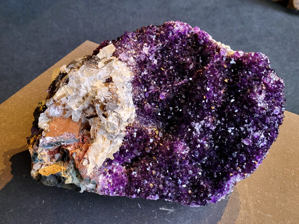 <strong>Amethist Cluster, Amethist, 6,6 kg, 390,- euro, nr. 2</strong>

Beschrijving Amethist.
<strong>Amethist is een paarse variëteit van kwarts, bekend om zijn kalmerende en spirituele eigenschappen. </strong>De kleur varieert van licht lila tot diep violet en wordt veroorzaakt door sporen van ijzer en andere elementen. Amethist wordt al eeuwenlang gewaardeerd, zowel vanwege zijn esthetische schoonheid als zijn vermeende genezende en beschermende krachten. 
Amethist is een kwartskristal, vaak te vinden in geodes (holtes in gesteente) of als afzonderlijke kristallen. 
<strong>De kleur varieert van lichtpaars tot diep violet, soms met roze of blauwe tinten. </strong>
De kleurintensiteit kan variëren, waarbij donkerdere amethisten vaak als kwalitatief worden beschouwd. 
Soms vertoont amethist dichroïsme, waarbij je verschillende kleuren kunt zien wanneer je de steen in het licht draait. 

<strong>Vindplaatsen:</strong>
Amethist wordt gevonden in verschillende delen van de wereld, waaronder Brazilië, Uruguay, Zambia, Madagaskar, Rusland en Canada.
Het wordt vaak gevonden in bergachtige gebieden. 
<strong>Gebruik:</strong>
Amethist wordt gebruikt in sieraden, decoratieve objecten en als helende steen. 
Het wordt vaak gedragen als hanger, ring of armband, of geplaatst in ruimtes om de energie te zuiveren. 
<strong>Amethist wordt ook gebruikt in meditatie en andere spirituele praktijken. </strong>