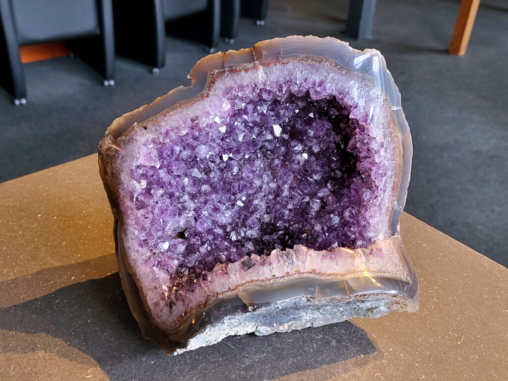 <strong>Amethist Cluster, Amethist in Agaat, 3,7 kg, 185,- euro, nr. 15</strong>

Beschrijving Amethist.
<strong>Amethist is een paarse variëteit van kwarts, bekend om zijn kalmerende en spirituele eigenschappen.</strong> De kleur varieert van licht lila tot diep violet en wordt veroorzaakt door sporen van ijzer en andere elementen. Amethist wordt al eeuwenlang gewaardeerd, zowel vanwege zijn esthetische schoonheid als zijn vermeende genezende en beschermende krachten. 
<strong>Amethist is een kwartskristal, vaak te vinden in geodes (holtes in gesteente) of als afzonderlijke kristallen. 
De kleur varieert van lichtpaars tot diep violet, soms met roze of blauwe tinten. </strong>
De kleurintensiteit kan variëren, waarbij donkerdere amethisten vaak als kwalitatief worden beschouwd. 
Soms vertoont amethist dichroïsme, waarbij je verschillende kleuren kunt zien wanneer je de steen in het licht draait. 

<strong>Vindplaatsen:</strong>
Amethist wordt gevonden in verschillende delen van de wereld, waaronder Brazilië, Uruguay, Zambia, Madagaskar, Rusland en Canada.
Het wordt vaak gevonden in bergachtige gebieden. 

<strong>Gebruik:</strong>
Amethist wordt gebruikt in sieraden, decoratieve objecten en als helende steen. 
Het wordt vaak gedragen als hanger, ring of armband, of geplaatst in ruimtes om de energie te zuiveren. 
<strong>Amethist wordt ook gebruikt in meditatie en andere spirituele praktijken. </strong>