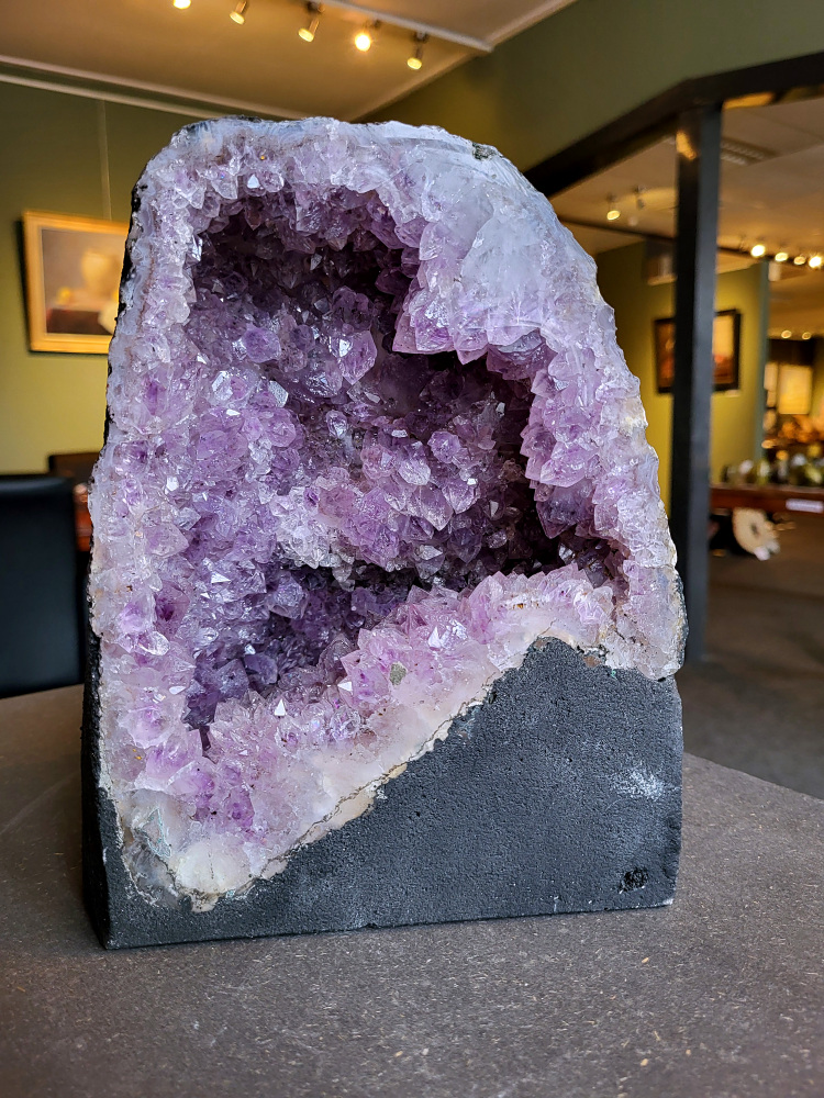 Amethist, Kunstgalerie Arnold, 7 kg, 70,- euro, nr. 11

Beschrijving Amethist.
Amethist is een paarse variëteit van kwarts, bekend om zijn kalmerende en spirituele eigenschappen. De kleur varieert van licht lila tot diep violet en wordt veroorzaakt door sporen van ijzer en andere elementen. Amethist wordt al eeuwenlang gewaardeerd, zowel vanwege zijn esthetische schoonheid als zijn vermeende genezende en beschermende krachten. 
Amethist is een kwartskristal, vaak te vinden in geodes (holtes in gesteente) of als afzonderlijke kristallen. 
De kleur varieert van lichtpaars tot diep violet, soms met roze of blauwe tinten. 
De kleurintensiteit kan variëren, waarbij donkerdere amethisten vaak als kwalitatief worden beschouwd. 
Soms vertoont amethist dichroïsme, waarbij je verschillende kleuren kunt zien wanneer je de steen in het licht draait. 

Vindplaatsen:
Amethist wordt gevonden in verschillende delen van de wereld, waaronder Brazilië, Uruguay, Zambia, Madagaskar, Rusland en Canada.
Het wordt vaak gevonden in bergachtige gebieden. 

Gebruik:
Amethist wordt gebruikt in sieraden, decoratieve objecten en als helende steen. 
Het wordt vaak gedragen als hanger, ring of armband, of geplaatst in ruimtes om de energie te zuiveren. 
Amethist wordt ook gebruikt in meditatie en andere spirituele praktijken. 
