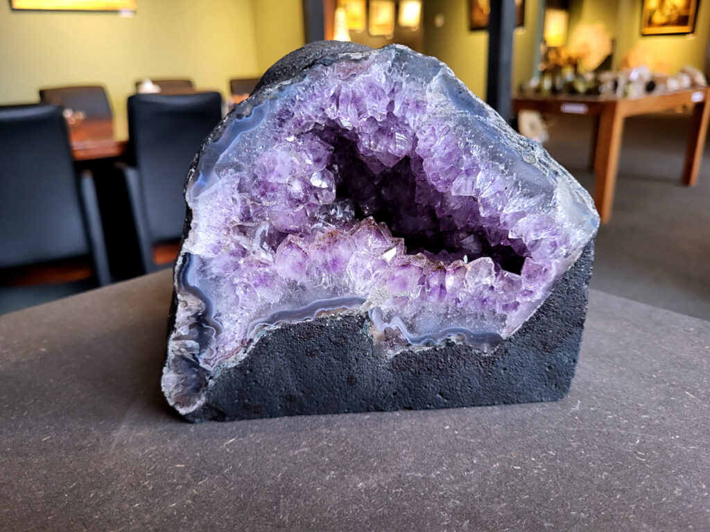 Amethist-Kunstgalerie-Arnold, Geode, 3,6kg, 36,- euro, nr. 19

Beschrijving Amethist.
Amethist is een paarse variëteit van kwarts, bekend om zijn kalmerende en spirituele eigenschappen. De kleur varieert van licht lila tot diep violet en wordt veroorzaakt door sporen van ijzer en andere elementen. Amethist wordt al eeuwenlang gewaardeerd, zowel vanwege zijn esthetische schoonheid als zijn vermeende genezende en beschermende krachten. 
Amethist is een kwartskristal, vaak te vinden in geodes (holtes in gesteente) of als afzonderlijke kristallen. 
De kleur varieert van lichtpaars tot diep violet, soms met roze of blauwe tinten. 
De kleurintensiteit kan variëren, waarbij donkerdere amethisten vaak als kwalitatief worden beschouwd. 
Soms vertoont amethist dichroïsme, waarbij je verschillende kleuren kunt zien wanneer je de steen in het licht draait. 

Vindplaatsen:
Amethist wordt gevonden in verschillende delen van de wereld, waaronder Brazilië, Uruguay, Zambia, Madagaskar, Rusland en Canada.
Het wordt vaak gevonden in bergachtige gebieden. 

Gebruik:
Amethist wordt gebruikt in sieraden, decoratieve objecten en als helende steen. 
Het wordt vaak gedragen als hanger, ring of armband, of geplaatst in ruimtes om de energie te zuiveren. 
Amethist wordt ook gebruikt in meditatie en andere spirituele praktijken. 
