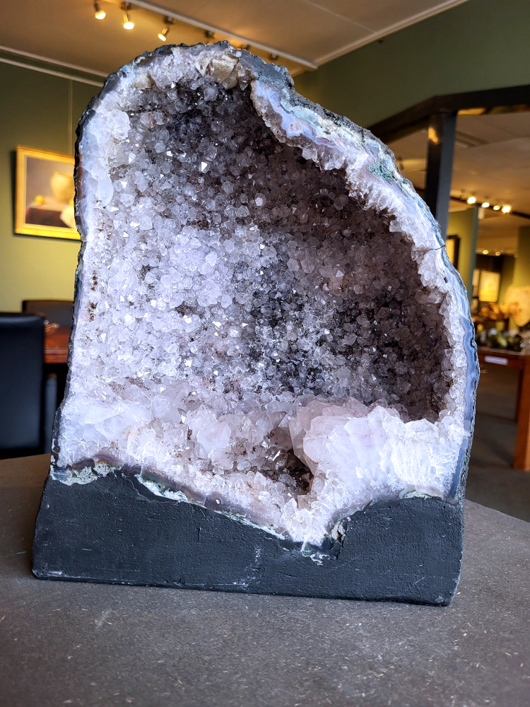 Amethist-Kunstgalerie-Arnold, Geode, 9,9 kg, 99,- euro, nr. 20

Beschrijving Amethist.
Amethist is een paarse variëteit van kwarts, bekend om zijn kalmerende en spirituele eigenschappen. De kleur varieert van licht lila tot diep violet en wordt veroorzaakt door sporen van ijzer en andere elementen. Amethist wordt al eeuwenlang gewaardeerd, zowel vanwege zijn esthetische schoonheid als zijn vermeende genezende en beschermende krachten. 
Amethist is een kwartskristal, vaak te vinden in geodes (holtes in gesteente) of als afzonderlijke kristallen. 
De kleur varieert van lichtpaars tot diep violet, soms met roze of blauwe tinten. 
De kleurintensiteit kan variëren, waarbij donkerdere amethisten vaak als kwalitatief worden beschouwd. 
Soms vertoont amethist dichroïsme, waarbij je verschillende kleuren kunt zien wanneer je de steen in het licht draait. 

Vindplaatsen:
Amethist wordt gevonden in verschillende delen van de wereld, waaronder Brazilië, Uruguay, Zambia, Madagaskar, Rusland en Canada.
Het wordt vaak gevonden in bergachtige gebieden. 

Gebruik:
Amethist wordt gebruikt in sieraden, decoratieve objecten en als helende steen. 
Het wordt vaak gedragen als hanger, ring of armband, of geplaatst in ruimtes om de energie te zuiveren. 
Amethist wordt ook gebruikt in meditatie en andere spirituele praktijken. 