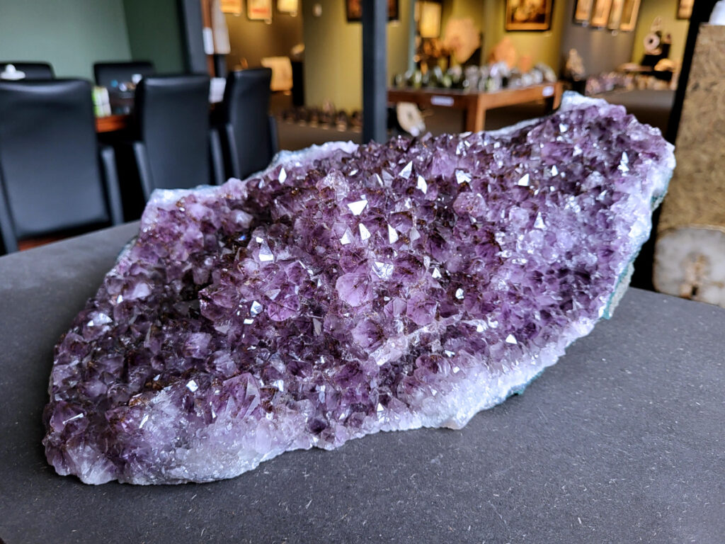 Amethist, druzy, cluster, geode, kunstgalerie arnold, 11,1kg, 395,- euro, nr. 7

Beschrijving Amethist.
Amethist is een paarse variëteit van kwarts, bekend om zijn kalmerende en spirituele eigenschappen. De kleur varieert van licht lila tot diep violet en wordt veroorzaakt door sporen van ijzer en andere elementen. Amethist wordt al eeuwenlang gewaardeerd, zowel vanwege zijn esthetische schoonheid als zijn vermeende genezende en beschermende krachten. 
Amethist is een kwartskristal, vaak te vinden in geodes (holtes in gesteente) of als afzonderlijke kristallen. 
De kleur varieert van lichtpaars tot diep violet, soms met roze of blauwe tinten. 
De kleurintensiteit kan variëren, waarbij donkerdere amethisten vaak als kwalitatief worden beschouwd. 
Soms vertoont amethist dichroïsme, waarbij je verschillende kleuren kunt zien wanneer je de steen in het licht draait. 

Vindplaatsen:
Amethist wordt gevonden in verschillende delen van de wereld, waaronder Brazilië, Uruguay, Zambia, Madagaskar, Rusland en Canada.
Het wordt vaak gevonden in bergachtige gebieden. 

Gebruik:
Amethist wordt gebruikt in sieraden, decoratieve objecten en als helende steen. 
Het wordt vaak gedragen als hanger, ring of armband, of geplaatst in ruimtes om de energie te zuiveren. 
Amethist wordt ook gebruikt in meditatie en andere spirituele praktijken. 