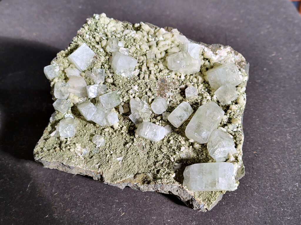 <strong>Apofyliet op matrix, 0,7 kg, 36,- euro, nr. 1</strong>

<strong>apofyliet op matrix</strong>
De doorzichtige tot melkachtige blokvormige kristallen zijn typisch voor apofyliet.
Apofyliet vormt vaak vierkante of rechthoekige kristallen met vlakke toppen.
De groenige korrelige ondergrond is een zeolietmatrix (bijvoorbeeld stilbiet of heulandiet).
Dit soort combinaties komt vaak uit India (Maharashtra regio).
<strong>Kenmerken van apofyliet</strong>
Kleur: transparant, wit, soms lichtgroen
<strong>Kristalvorm: </strong>kubusachtig / blokvormig met glanzende vlakken
<strong>Glans: glasachtig</strong>
Vaak gevonden samen met: stilbiet, heulandiet, calciet
<strong>Apofyliet is een helder of wit mineraal dat behoort tot de groep van de calciumsilicaten.</strong> Het wordt voornamelijk gevonden in vulkanische gesteenten, vooral in de buurt van breuken en scheuren. In de spirituele wereld wordt Apofyliet beschouwd als een krachtige steen met een hoge vibratie die helpt bij het openen en activeren van de hogere chakra's, met name het derde oog en de kruinchakra.
<strong>Apofyliet werkt ondersteunend bij innerlijke druk en angsten, tevens goede steen om fixaties en rigiditeit los te laten.</strong> De steen spoort je aan om je thuis te voelen in je eigen lichaam. Dit maakt het een zeer goede steen voor meditatieve doeleinden. De energie van Apofyliet wordt ook geassocieerd met helderheid, zuiverheid en zuivering. Het kan worden gebruikt om negatieve energieën en emoties te verwijderen en om een gevoel van kalmte en vrede te bevorderen. Het kan ook helpen bij het verminderen van stress en angst en het bevorderen van innerlijke rust en harmonie.
Fysiek wordt Apofyliet geassocieerd met het versterken van het immuunsysteem en het bevorderen van een gezonde spijsvertering. Het kan ook worden gebruikt om hoofdpijn, migraine en andere pijnlijke aandoeningen te verlichten. Het loslaten van fixaties en rigiditeit kan ook verlichting bieden voor fysieke spanning in het lichaam.
<strong>Over het algemeen wordt Apofyliet beschouwd als een krachtige steen voor spirituele groei en genezing, en het kan een waardevolle aanvulling zijn op meditatie- en genezingspraktijken.</strong> Het biedt emotionele en mentale ondersteuning door het helpen loslaten van fixaties en rigiditeit, en het bevorderen van innerlijke rust en harmonie. Het biedt ook fysieke voordelen, zoals het versterken van het immuunsysteem en het verlichten van hoofdpijn en andere pijnlijke aandoeningen.