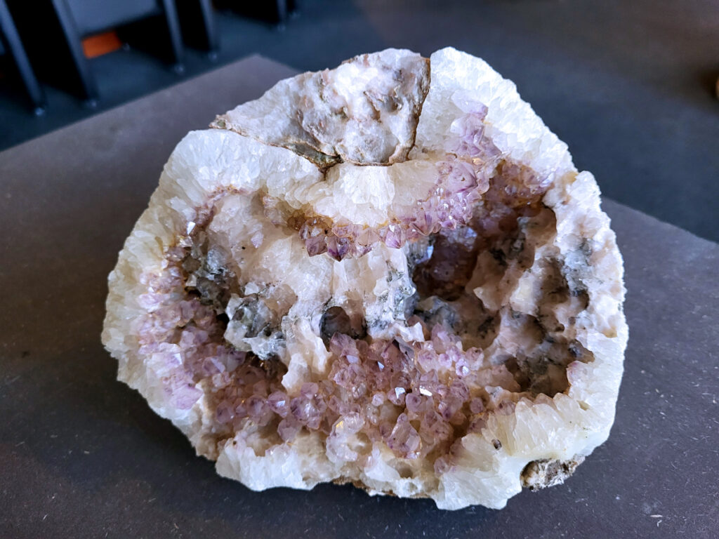 Chalcedoon Geode, Cluster, Amethist, 2,6 kg, 50,- euro, nr. 5

Chalcedoon geode met druzy kristallen.
Geodes ontstaan in holtes van gesteente (vaak vulkanisch). Mineralenrijk water vult die holte en kristalliseert langzaam, waardoor die fijne kristalletjes groeien.

De buitenkant is ruw en gesteente achtig, dat is de “schil” van de geode.
Binnenin zit een holte en dat is typisch voor een geode.
De binnenkant is bedekt met kleine, glinsterende kristalletjes en dat noem je druzy (druze).
De lichtblauwe/groene tint wijst op chalcedoon, een microkristallijne vorm van kwarts.
Kenmerken:
Materiaal: chalcedoon (kwartsfamilie)
Structuur: geode met druzy coating
Kleur: wit tot licht blauw/groen
Glans: suikerachtig, sprankelend

Vergelijkbaar met:
Agaat-geodes (maar die hebben vaak duidelijke banden)
Kwarts-geodes (meestal grotere, puntige kristallen i.p.v. fijne druzy)