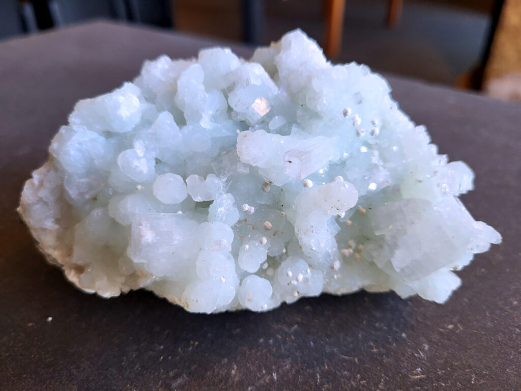 Chalcedoon geode met druzy kristallen, 0,4, 13,- euro, nr. 3

Chalcedoon geode met druzy kristallen.
Geodes ontstaan in holtes van gesteente (vaak vulkanisch). Mineralenrijk water vult die holte en kristalliseert langzaam, waardoor die fijne kristalletjes groeien.

De buitenkant is ruw en gesteente achtig, dat is de “schil” van de geode.
Binnenin zit een holte en dat is typisch voor een geode.
De binnenkant is bedekt met kleine, glinsterende kristalletjes en dat noem je druzy (druze).
De lichtblauwe/groene tint wijst op chalcedoon, een microkristallijne vorm van kwarts.
Kenmerken:
Materiaal: chalcedoon (kwartsfamilie)
Structuur: geode met druzy coating
Kleur: wit tot licht blauw/groen
Glans: suikerachtig, sprankelend

Vergelijkbaar met:
Agaat-geodes (maar die hebben vaak duidelijke banden)
Kwarts-geodes (meestal grotere, puntige kristallen i.p.v. fijne druzy)