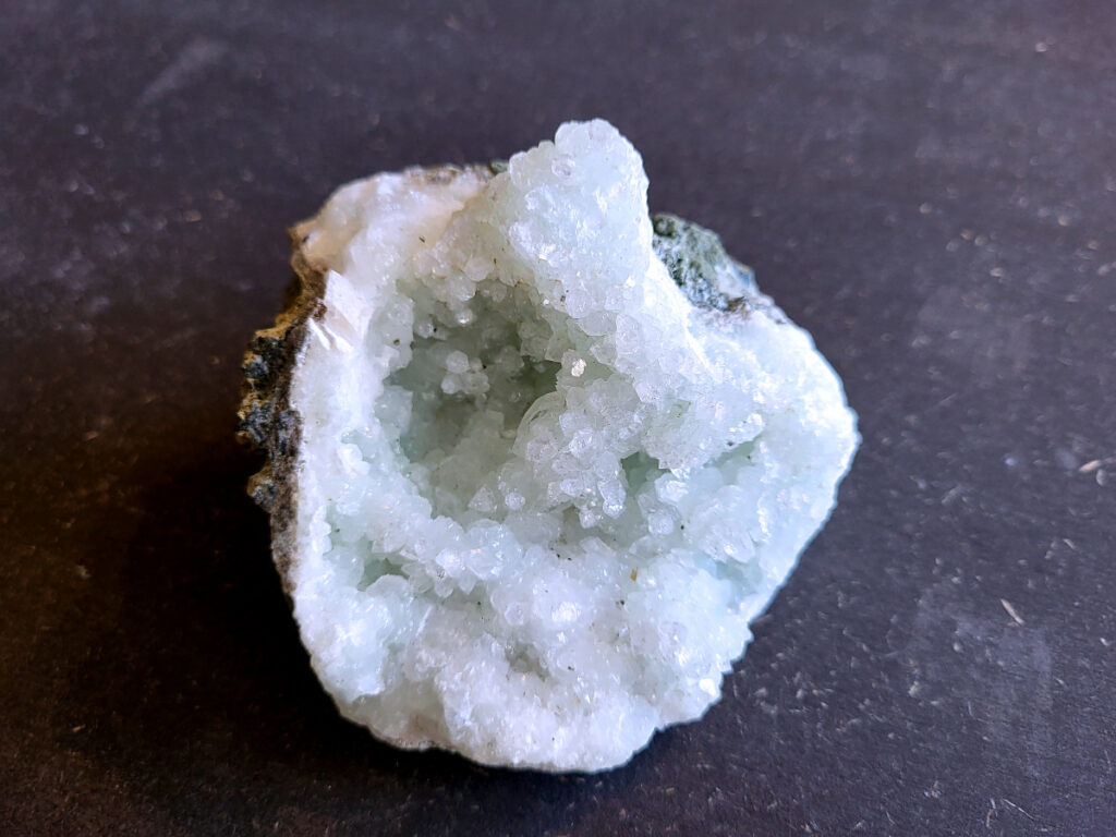 Chalcedoon geode met druzy kristallen, 0,4 kg, 12,- euro, nr. 4

Chalcedoon geode met druzy kristallen.
Geodes ontstaan in holtes van gesteente (vaak vulkanisch). Mineralenrijk water vult die holte en kristalliseert langzaam, waardoor die fijne kristalletjes groeien.

De buitenkant is ruw en gesteente achtig, dat is de “schil” van de geode.
Binnenin zit een holte en dat is typisch voor een geode.
De binnenkant is bedekt met kleine, glinsterende kristalletjes en dat noem je druzy (druze).
De lichtblauwe/groene tint wijst op chalcedoon, een microkristallijne vorm van kwarts.
Kenmerken:
Materiaal: chalcedoon (kwartsfamilie)
Structuur: geode met druzy coating
Kleur: wit tot licht blauw/groen
Glans: suikerachtig, sprankelend

Vergelijkbaar met:
Agaat-geodes (maar die hebben vaak duidelijke banden)
Kwarts-geodes (meestal grotere, puntige kristallen i.p.v. fijne druzy)