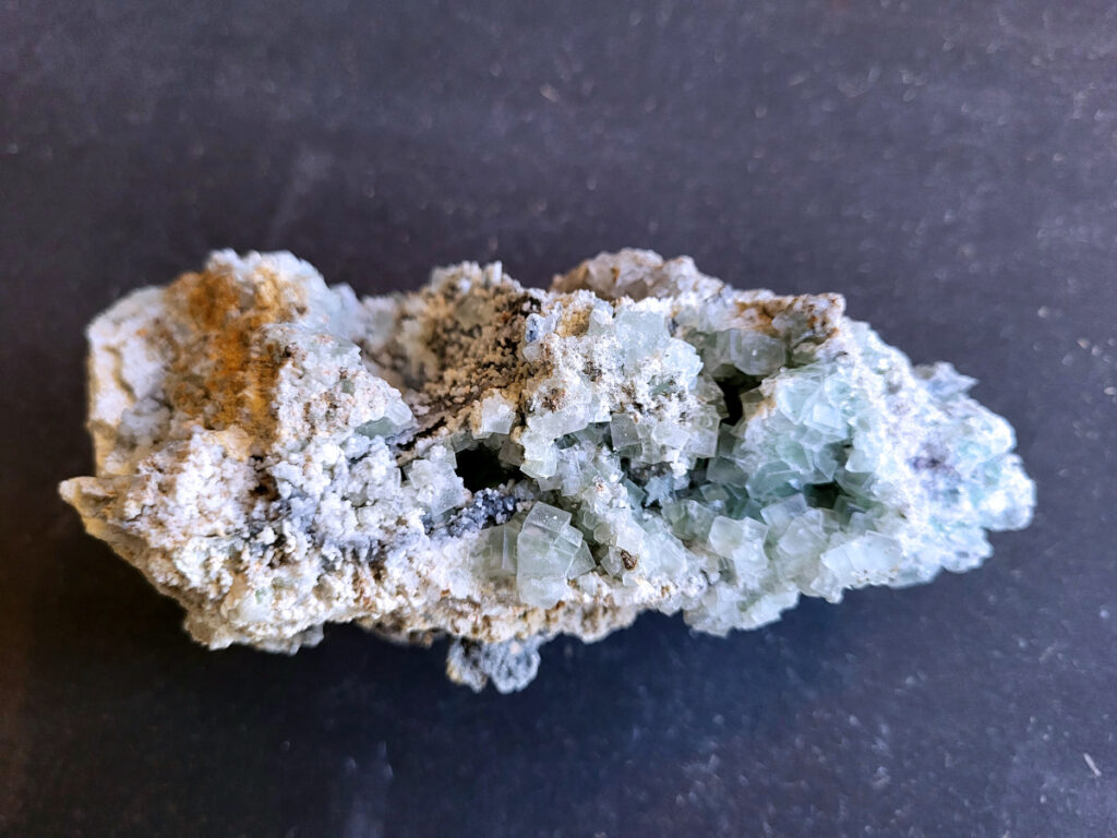 Chalcedoon geode met druzy kristallen, 0,7 kg, 21,- euro, nr. 1

Chalcedoon geode met druzy kristallen.
Geodes ontstaan in holtes van gesteente (vaak vulkanisch). Mineralenrijk water vult die holte en kristalliseert langzaam, waardoor die fijne kristalletjes groeien.

De buitenkant is ruw en gesteente achtig, dat is de “schil” van de geode.
Binnenin zit een holte en dat is typisch voor een geode.
De binnenkant is bedekt met kleine, glinsterende kristalletjes en dat noem je druzy (druze).
De lichtblauwe/groene tint wijst op chalcedoon, een microkristallijne vorm van kwarts.
Kenmerken:
Materiaal: chalcedoon (kwartsfamilie)
Structuur: geode met druzy coating
Kleur: wit tot licht blauw/groen
Glans: suikerachtig, sprankelend

Vergelijkbaar met:
Agaat-geodes (maar die hebben vaak duidelijke banden)
Kwarts-geodes (meestal grotere, puntige kristallen i.p.v. fijne druzy)