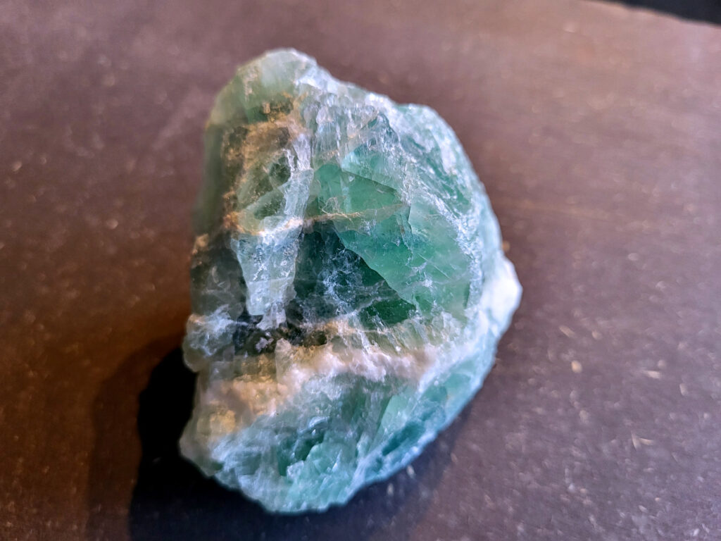 <strong>Fluoriet, brok groene fluoriet, 0,5 kg, 15,- euro, nr. 1</strong>

Fluoriet,
<strong>Fluoriet is een veelzijdig, kleurrijk mineraal (calciumfluoride) dat bekend staat om zijn sterke concentratie bevorderende, beschermende en reinigende werking op de geest. </strong>Het ordent chaos, helpt bij studie en emotionele stabiliteit, en wordt vaak gebruikt om elektromagnetische straling te verminderen. Het mineraal fluoresceert vaak onder UV-licht.
<strong>Kernmerken van Fluoriet:</strong>
<strong>Kleur:</strong> Zeer variabel, inclusief paars, groen, blauw, geel en kleurloos.
Hardheid: 4 op de schaal van Mohs (tamelijk zacht).
<strong>Kristalstelsel:</strong> Kubisch, vaak als octaëder.
<strong>Toepassing: </strong>Geliefd bij verzamelaars, spirituele beoefenaars (meditatie) en industrieel gebruikt als vloeispaat (vloeimiddel bij metaalsmelting).
<strong>Spirituele en Emotionele Werking:</strong>
<strong>Focus & Studie:</strong> Helpt bij het ordenen van gedachten, concentratie en snelle informatieverwerking.
<strong>Bescherming:</strong> Werkt stabiliserend, vergroot het zelfvertrouwen en helpt tegen negatieve invloeden of overprikkeling.
<strong>Emotionele balans: </strong>Brengt emoties in evenwicht en helpt bij het loslaten van oude patronen. 
Fysieke Werking (Edelsteentherapie):
<strong>Botten en Gebit:</strong> Ondersteunt de gezondheid van tanden, botten en gewrichten.
<strong>Pijnbestrijding:</strong> Wordt ingezet bij zenuwpijn, gordelroos en artritis.
<strong>Reiniging:</strong> Zou helpen bij ontgifting en het immuunsysteem versterken. 

Kleurvariaties en Specifieke Werking:
<strong>Groene Fluoriet:</strong> Reinigt de aura, bevordert emotionele healing en nuchterheid.
<strong>Paarse Fluoriet: </strong>Stimuleert de intuïtie en spirituele wijsheid.
<strong>Blauwe Fluoriet:</strong> Ondersteunt communicatie en creativiteit.
<strong>Regenboogfluoriet:</strong> Combineert de eigenschappen van de verschillende kleuren.