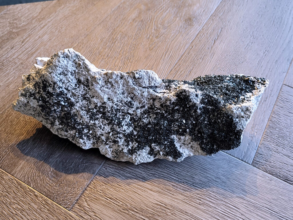 <strong>Kwarts, Druzy Kwarts, 1 kg, 10,- euro, nr. 2</strong>

Kwarts, Druzy Kwarts op een matrix van Calciet

<strong>Druzy kwarts op een matrix van calciet (waarschijnlijk ijzer/mangaan-oxiden).</strong>
De donkere kleine kwartskristalletjes (druzy) glinsteren je tegemoet.
De ondergrond is wit/grijs en dat is typisch voor calciet 
<strong>De donkere kleur komt vaak door mineralen zoals hematiet of mangaan die tijdens de vorming in de kwarts zijn gekomen.</strong>
Druzy kwarts op calciet met donkere mineralisatie.
Met een sterke glitter. Dat is typisch druzy.
<strong>Spiritueel :
Druzy kwarts wordt vaak gezien als versterker van energie en helderheid.
Door de donkere mineralen wordt hij soms gezien als beschermend / aardend.
Zulke natuurlijke stukken komen vaak uit Marokko of China.
</strong>