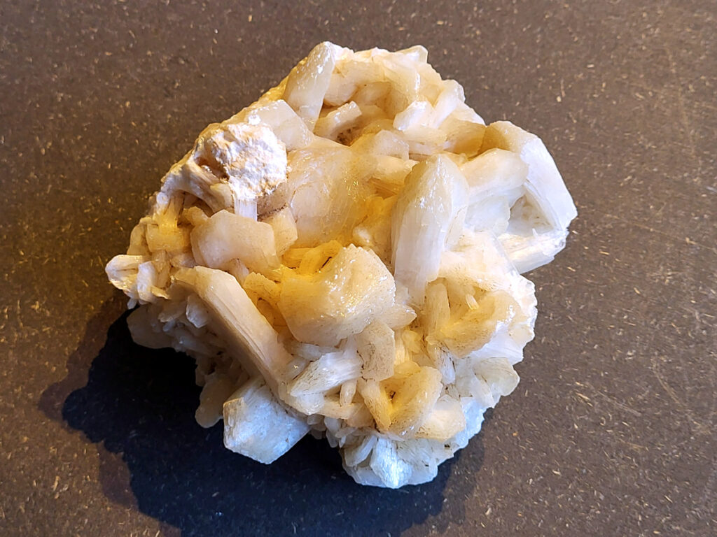 <strong>Stilbiet Cluster, 0,6 kg, 13,- euro, nr. 3</strong>

Stilbiet,
<strong>De waaier- of bundelvormige kristallen met een zijdeachtige glans en soms lichtgroen-geelatige gloed zijn typisch voor stilbiet.</strong>
De helder witte tot doorschijnende kubusvormige kristallen aan de basis zijn apofyliet.
De gele of groenige zweem kan komen van een lichte epidoot- of prehniet-insluiting, of een natuurlijke oxidatie aan het oppervlak.
Energetische werking:
<strong>Stilbiet opent het hart en helpt loslaten van zorgen; het is zacht, troostend en bevordert vertrouwen in de loop van het leven.</strong>
Apofyliet versterkt intuïtie, helderheid en spirituele verbinding — een “lichtbrenger” die energie zuivert in een ruimte.
Samen vormen ze een kalmerende, hoogtrillende combinatie die ideaal is voor meditatie, healingruimtes of slaapkamers (voor rust en inzicht).
Zorgtip:
Houd ze uit direct zonlicht (kan verkleuren) en reinig liever met klank, maanlicht of wierook in plaats van water — apofyliet lost iets op bij langdurig vocht.
<strong> Uiterlijk:</strong>
De perzik- tot crème-witte kleur,
De glanzende, waaier- of bloemvormige kristalstructuur,
De zachte, zijdeachtige glans (bijna parelmoerachtig),
al die kenmerken passen heel goed bij stilbiet.
De ronde, lichtgrijze korrelige bol bovenop kan een heulandiet- of chalcedoon-vorming zijn die samen met de stilbiet is gegroeid.
Energetische betekenis:
<strong>Stilbiet hoort bij het hart en het kruinchakra — een zachte, troostende energie die helpt bij het loslaten van oude patronen en het verbinden met hogere leiding.
Ze ondersteunt intuïtie, dromen en zachtheid in relaties — een heel liefdevolle steen om in huis te hebben, vooral bij healing- of slaapruimtes.</strong>