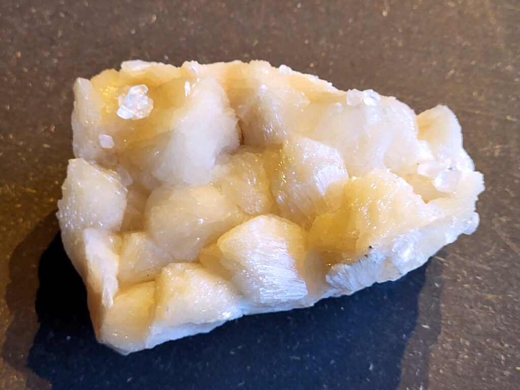 <strong>Stilbiet Cluster, 0,6 kg, 13,- euro, nr. 4</strong>

Stilbiet,
<strong>De waaier- of bundelvormige kristallen met een zijdeachtige glans en soms lichtgroen-geelatige gloed zijn typisch voor stilbiet.</strong>
De helder witte tot doorschijnende kubusvormige kristallen aan de basis zijn apofyliet.
De gele of groenige zweem kan komen van een lichte epidoot- of prehniet-insluiting, of een natuurlijke oxidatie aan het oppervlak.
Energetische werking:
<strong>Stilbiet opent het hart en helpt loslaten van zorgen; het is zacht, troostend en bevordert vertrouwen in de loop van het leven.</strong>
Apofyliet versterkt intuïtie, helderheid en spirituele verbinding — een “lichtbrenger” die energie zuivert in een ruimte.
Samen vormen ze een kalmerende, hoogtrillende combinatie die ideaal is voor meditatie, healingruimtes of slaapkamers (voor rust en inzicht).
Zorgtip:
Houd ze uit direct zonlicht (kan verkleuren) en reinig liever met klank, maanlicht of wierook in plaats van water — apofyliet lost iets op bij langdurig vocht.
<strong> Uiterlijk:</strong>
De perzik- tot crème-witte kleur,
De glanzende, waaier- of bloemvormige kristalstructuur,
De zachte, zijdeachtige glans (bijna parelmoerachtig),
al die kenmerken passen heel goed bij stilbiet.
De ronde, lichtgrijze korrelige bol bovenop kan een heulandiet- of chalcedoon-vorming zijn die samen met de stilbiet is gegroeid.
Energetische betekenis:
<strong>Stilbiet hoort bij het hart en het kruinchakra — een zachte, troostende energie die helpt bij het loslaten van oude patronen en het verbinden met hogere leiding.
Ze ondersteunt intuïtie, dromen en zachtheid in relaties — een heel liefdevolle steen om in huis te hebben, vooral bij healing- of slaapruimtes.
</strong>